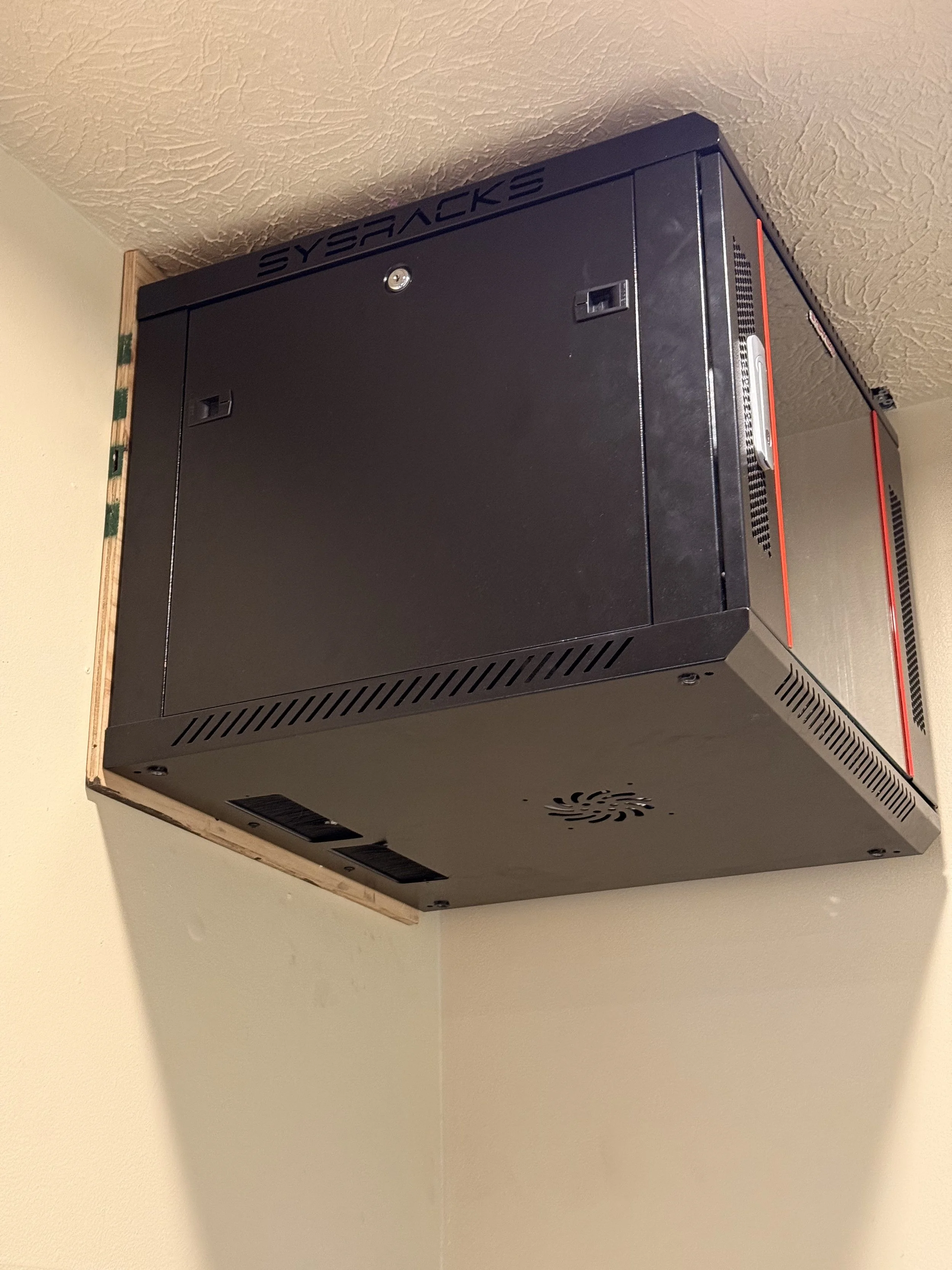 A black mining or industrial computer mounted on a wall, with the brand name 'SYERACKS' on top, and ventilation holes and slots on the sides.