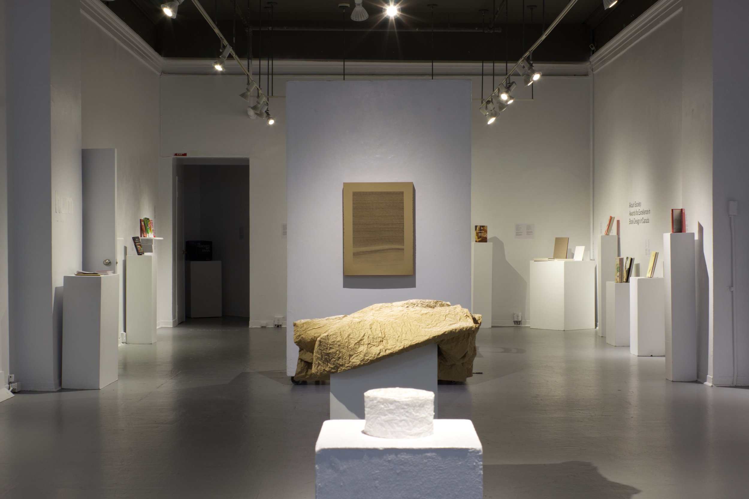 Inside a gallery with two abstract sculputers in line with a drawing mounted on the wall.