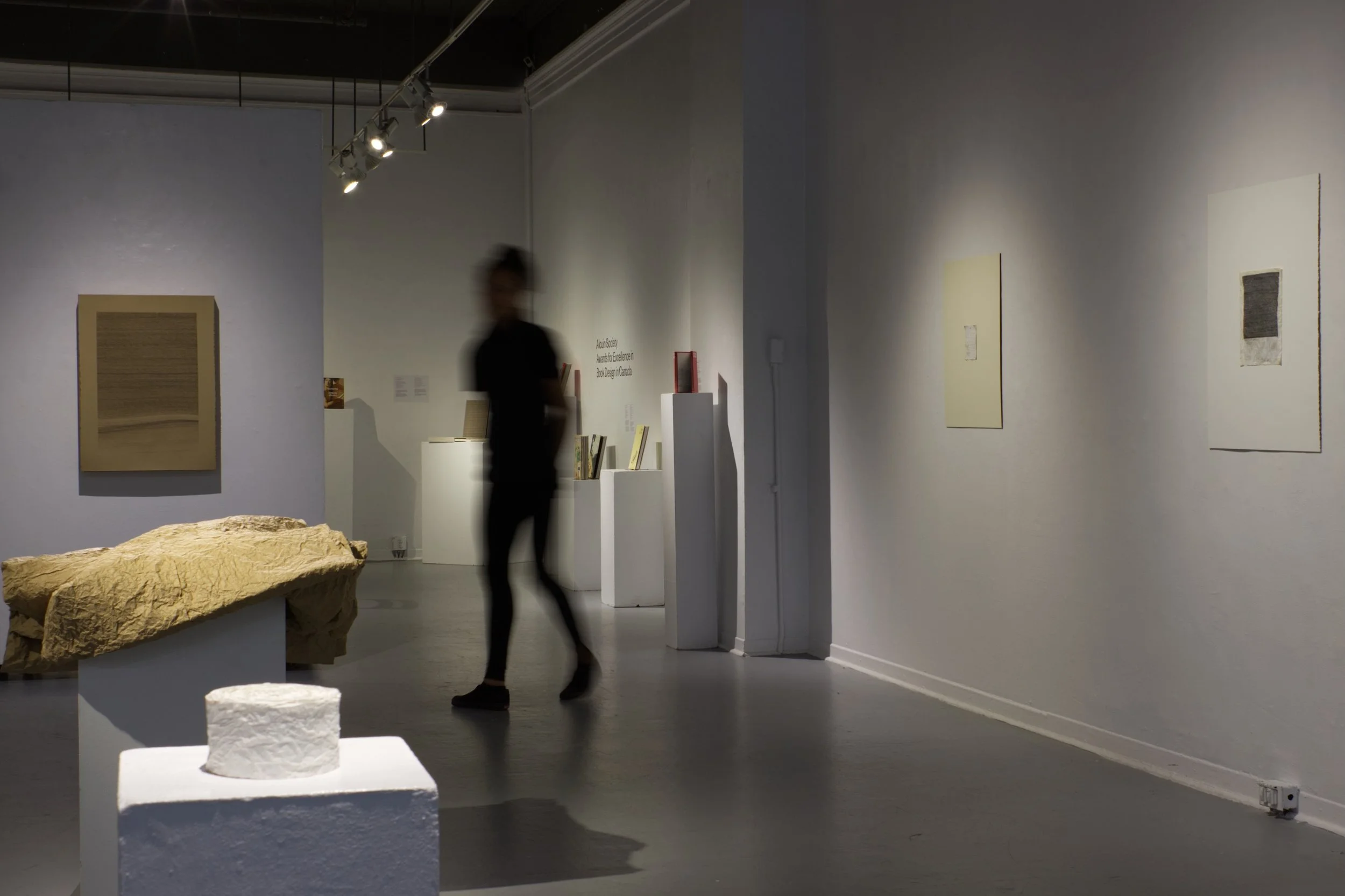 A blurred figure moves through the gallery space amidst the exhibition.
