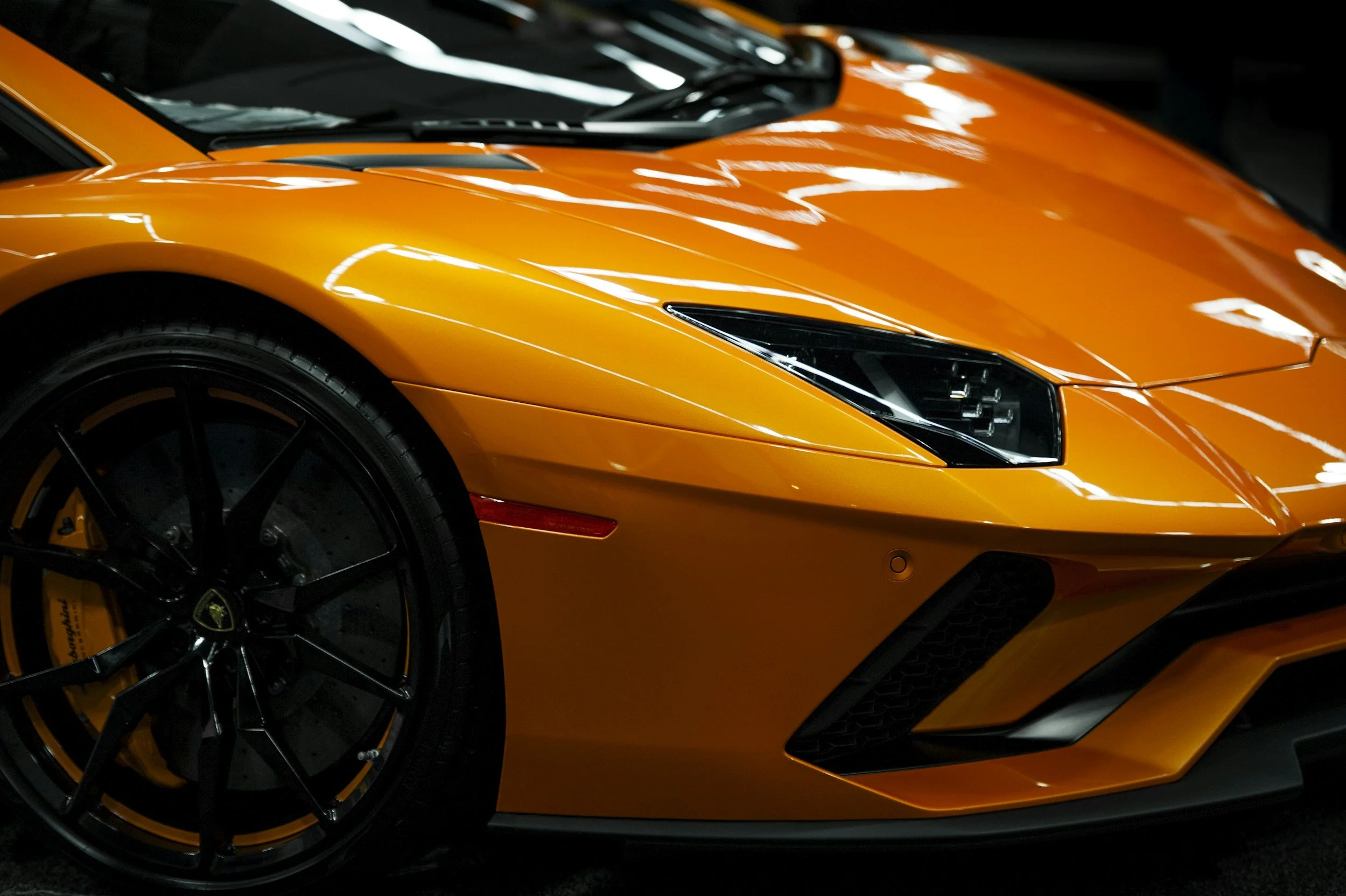 Ceramic Coating. Close-up of an orange sports car, focusing on the front left side, including the tire, headlight, and part of the hood.