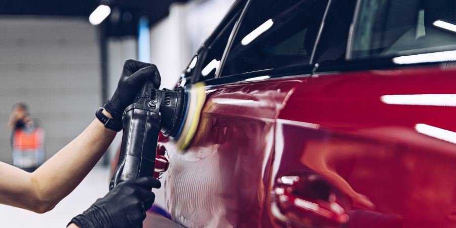 A person polishing a red car with a buffer in an indoor garage or workshop.
