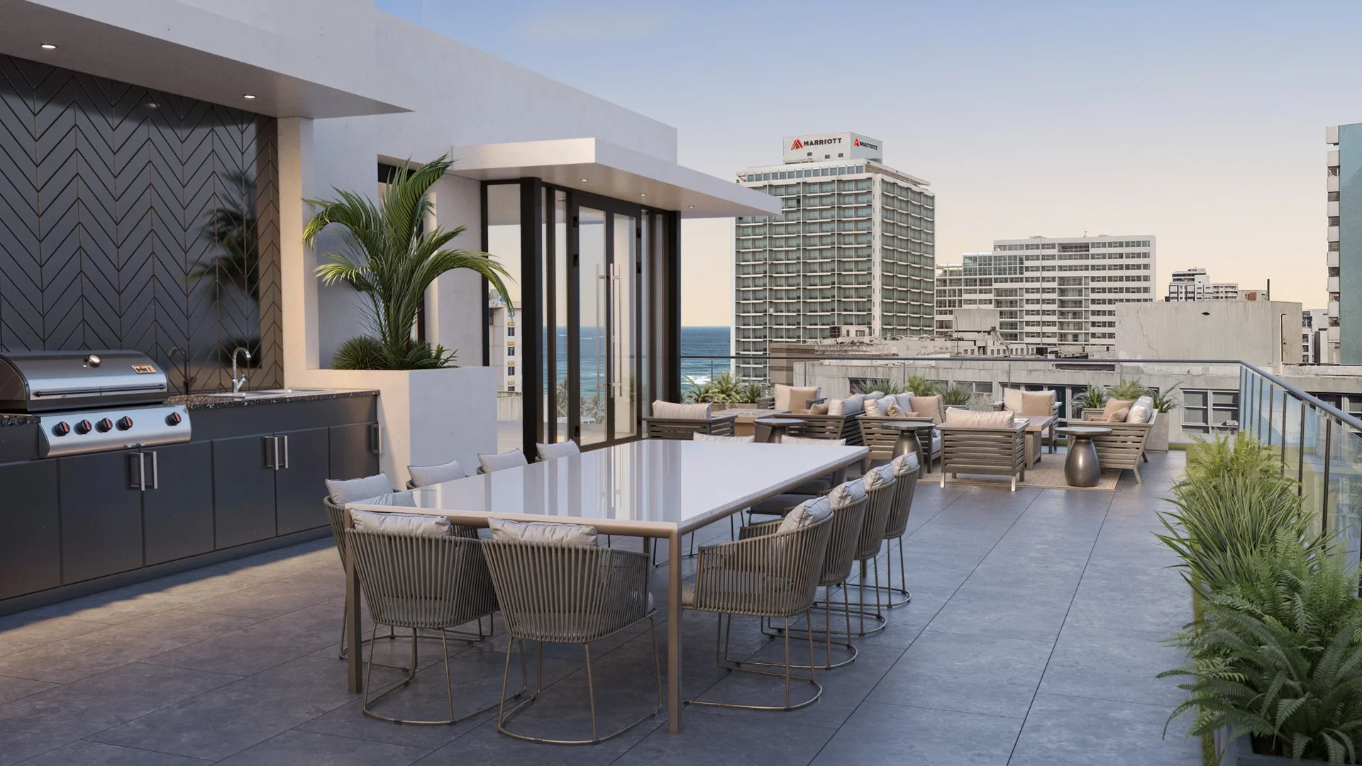 Rooftop terrace with a dining table, outdoor seating area, grill, and plants, overlooking a cityscape and ocean in the distance.