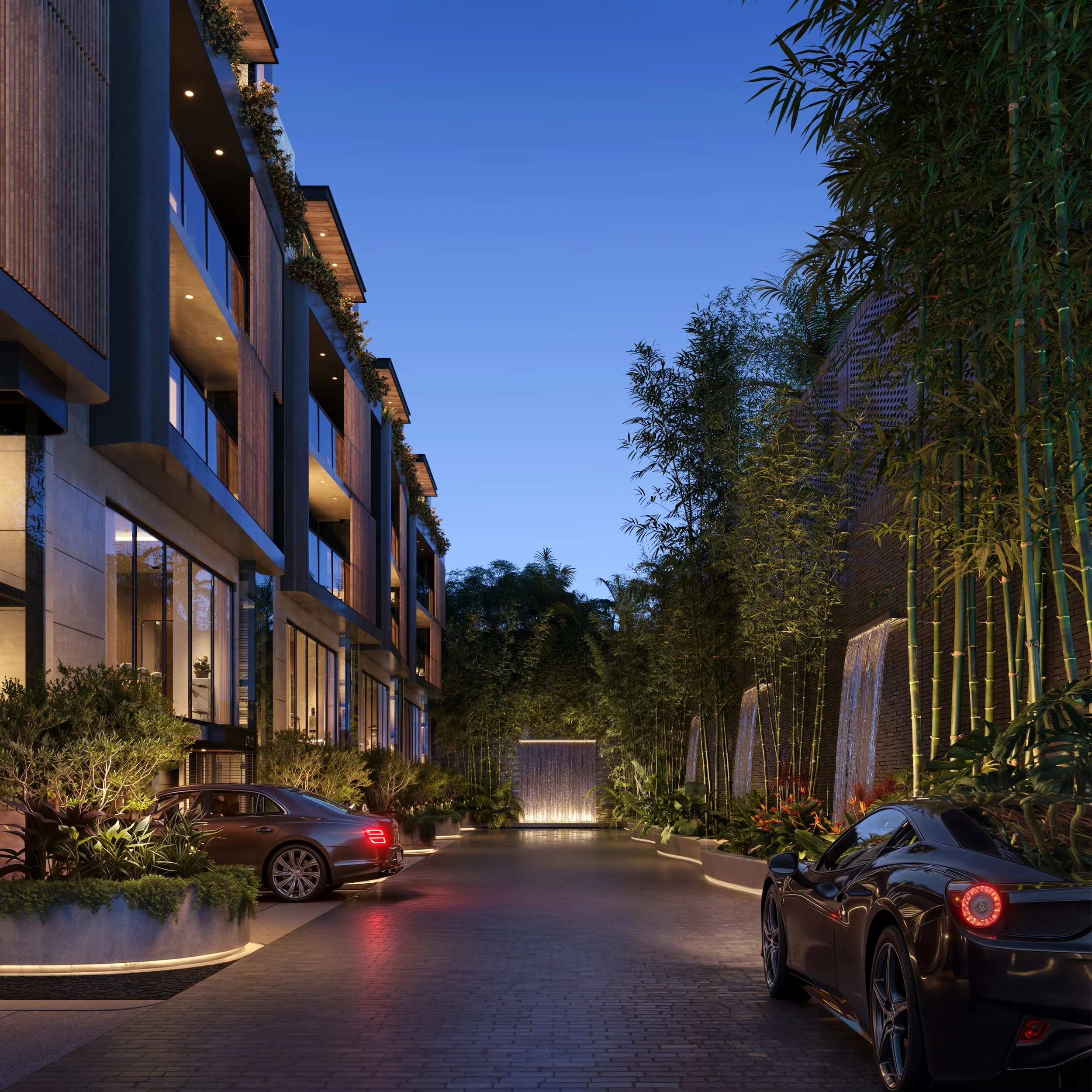 Luxury apartment complex driveway with two parked cars, lush landscaping, and waterfalls on the right, illuminated at dusk.