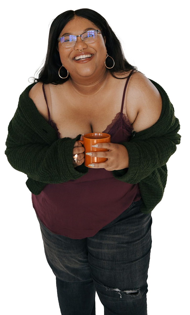 A woman with black hair, glasses, and hoop earrings, smiling, holding an orange mug, wearing a maroon top, green cardigan, and dark jeans.