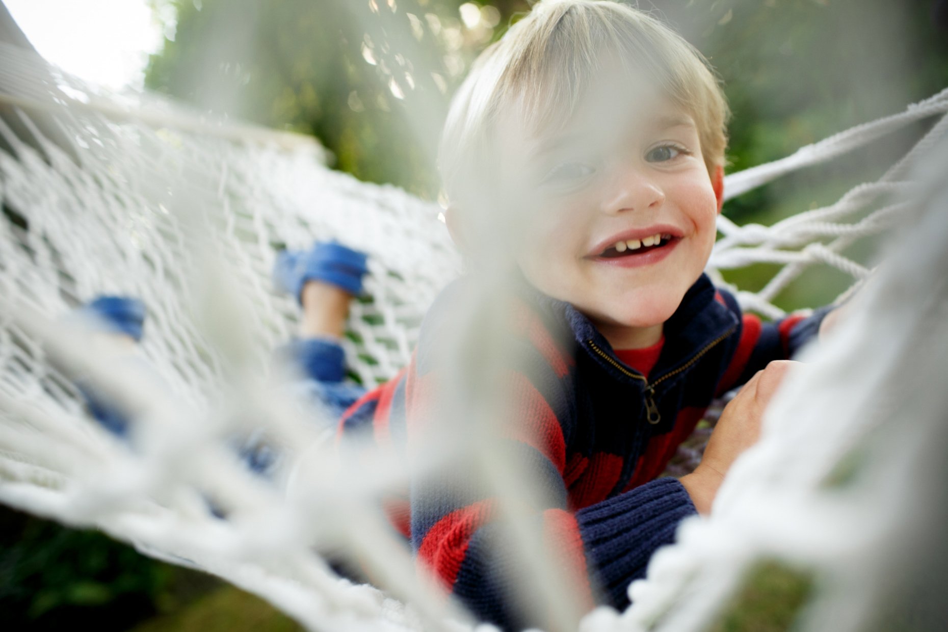 Young boy smiling and lying down on a hammock outdoors, smiling at the camera.