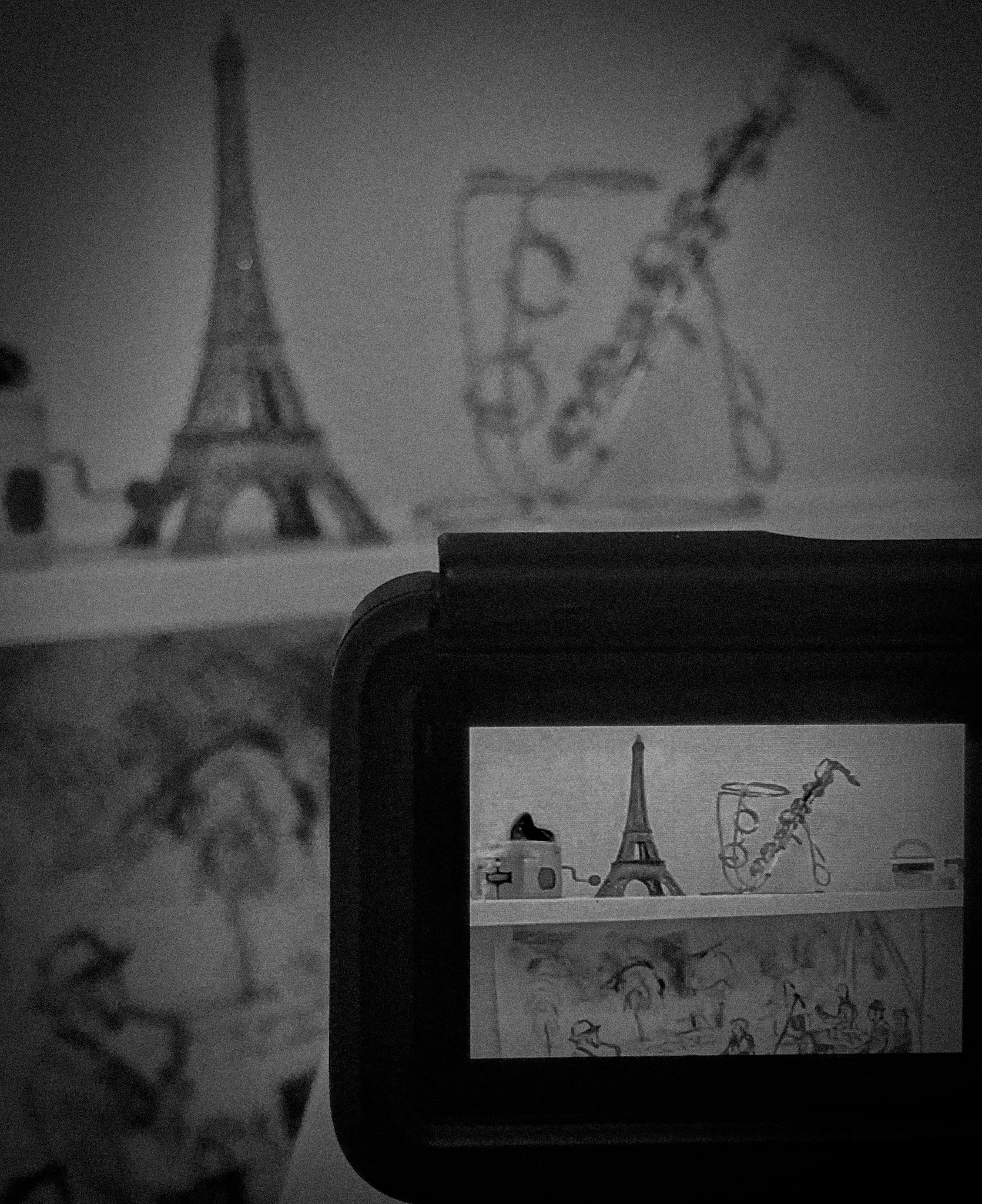 Teléfono móvil tomando una foto de dibujos en la pared, incluyendo la Torre Eiffel, un esqueleto y un saxofón, en un entorno de habitación