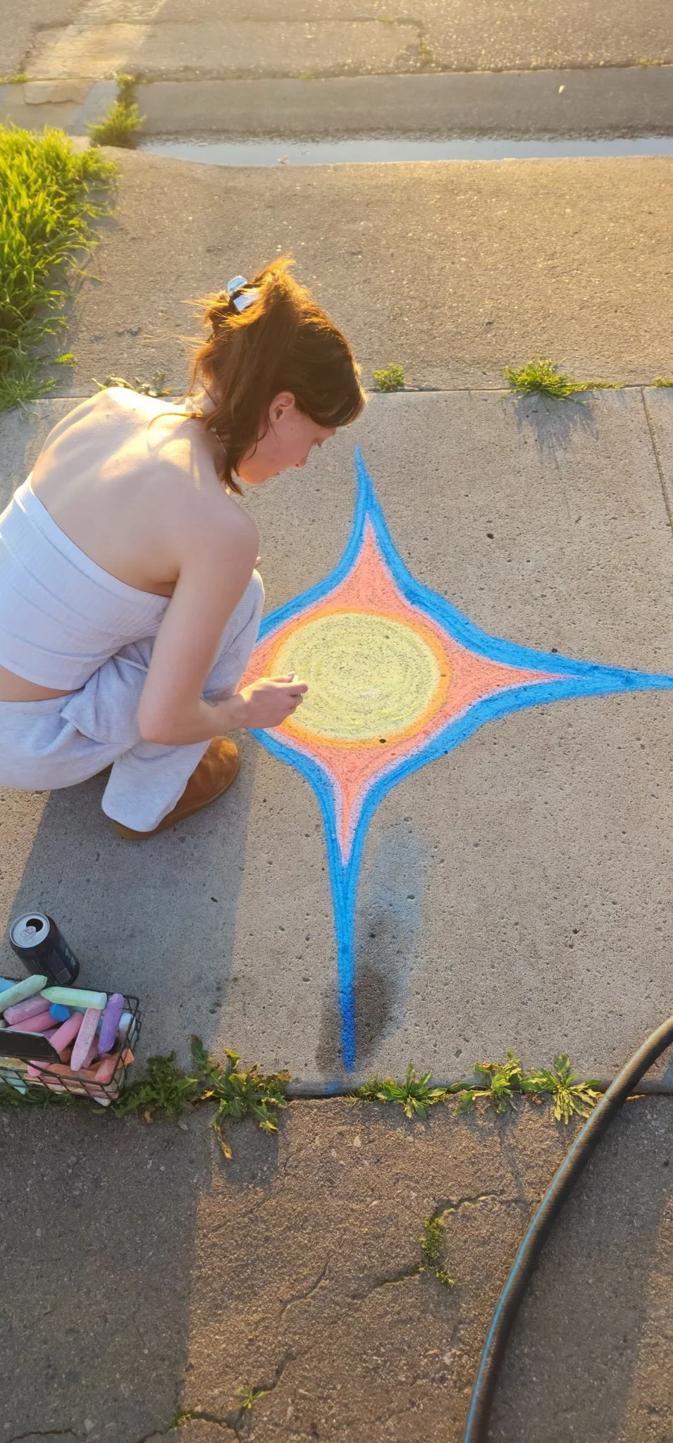 Woman drawing colorful chalk artwork on concrete sidewalk during sunset.