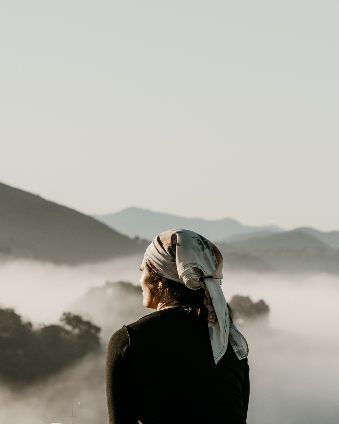A woman wearing a headscarf gazing at misty mountains and trees.