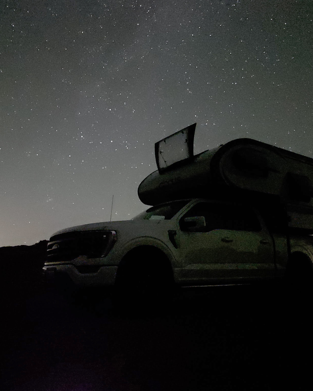 A pickup truck parked in a dark area at night, with a clear starry sky overhead.