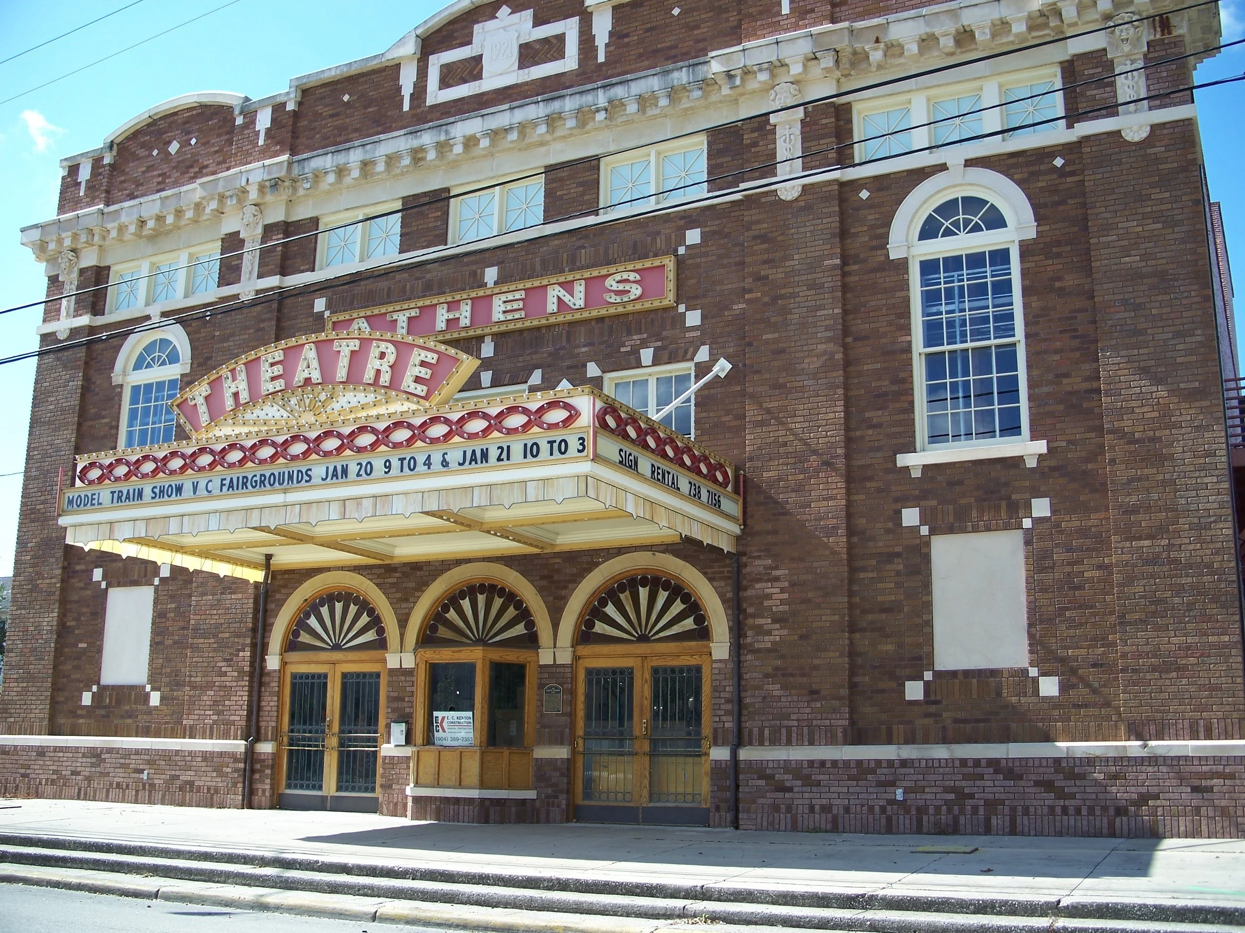 Front of the Athens Theatre, a brick building with arched windows and an illuminated marquee advertising a model train show at the fairgrounds from January 20 to January 21 with hours from 9 to 4 and 10 to 3.