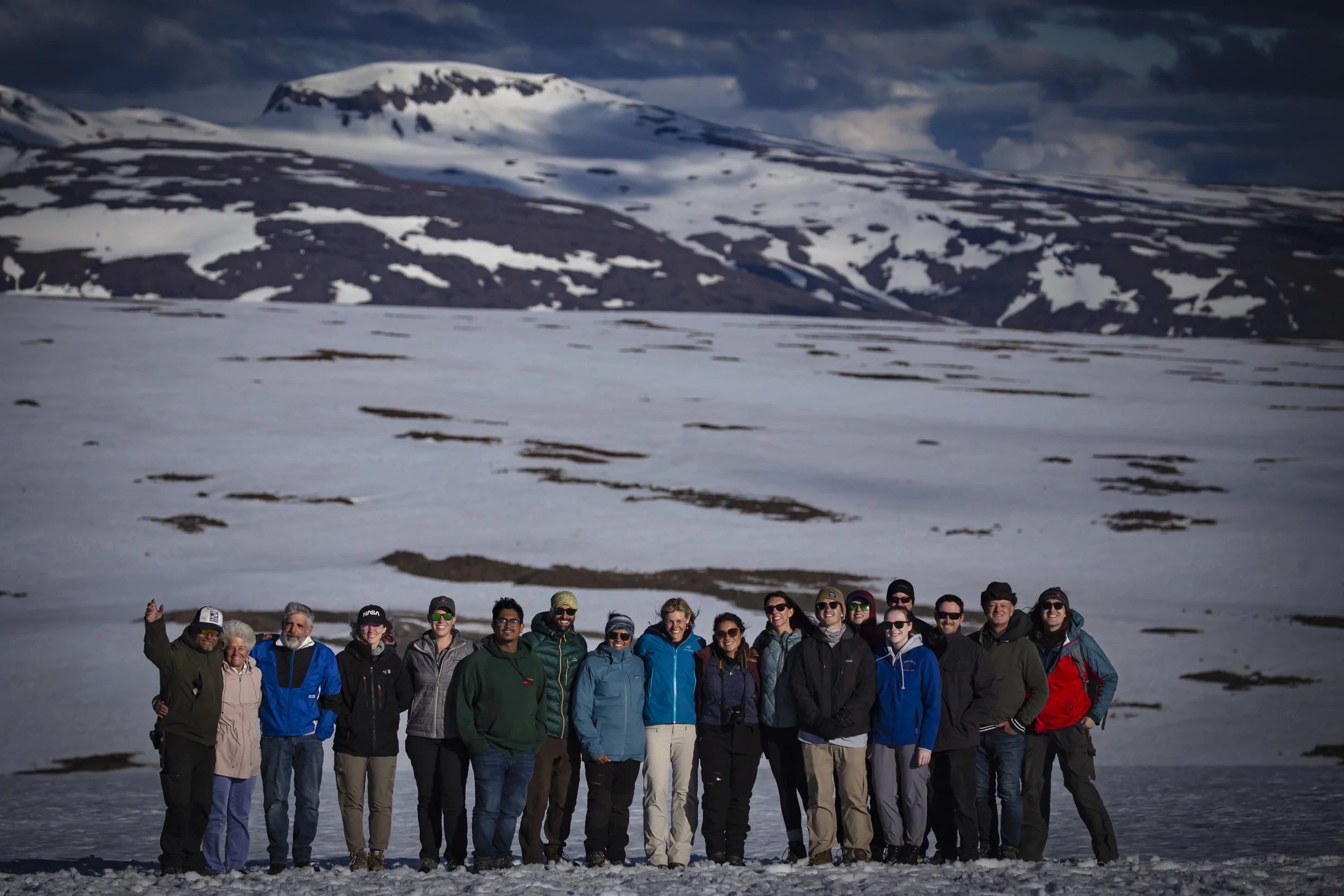 Group of people standing on snowy terrain with snow-covered mountains in the background