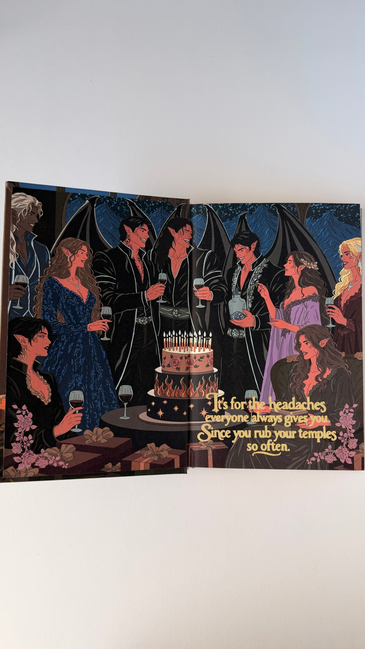 The book open at the front endpaper: the Solstice celebration, friends raising glasses around a candlelit cake, running across both boards.