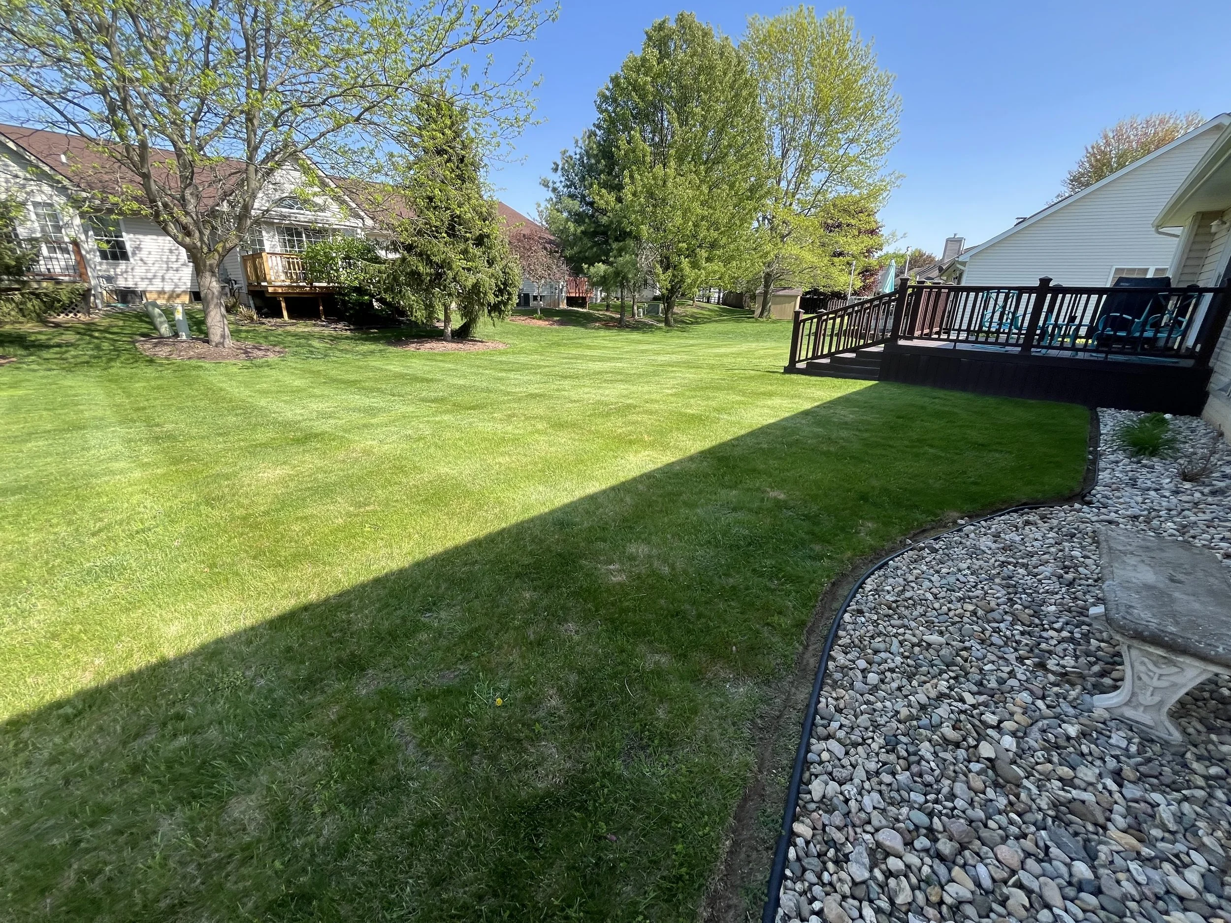 Backyard lawn with crisp edging, trimmed grass, and maintained rock landscaping in Tecumseh Michigan.