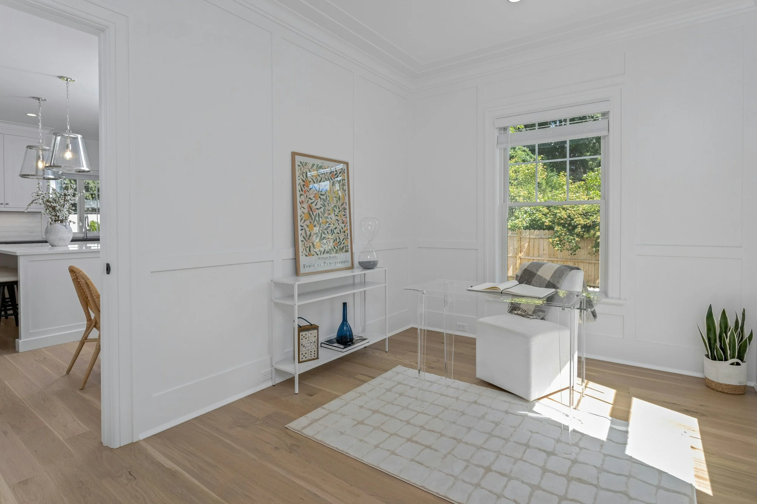 Bright living room with large window, white walls, and wooden floor, decorated with minimal furniture and plants.