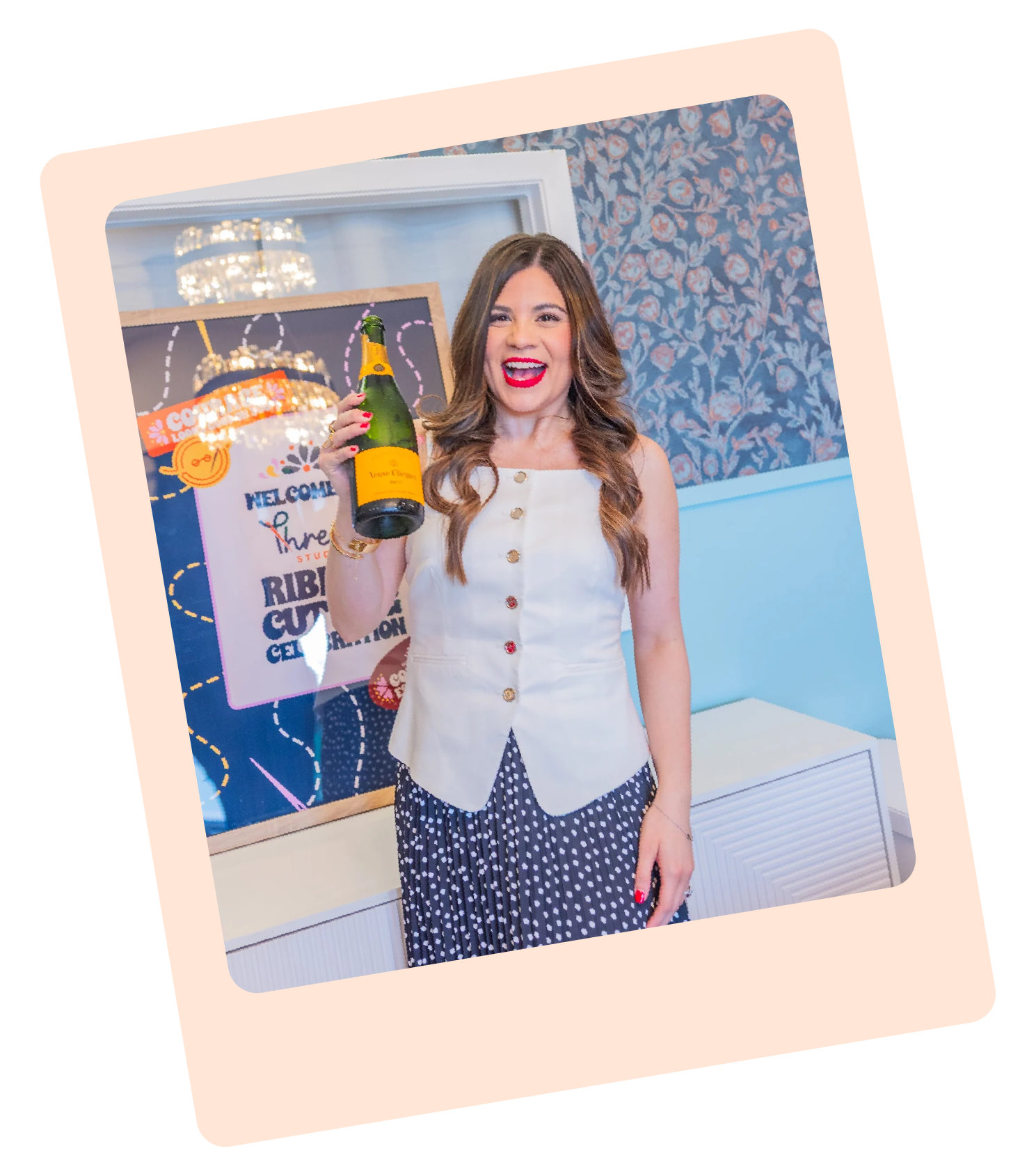 A polaroid style photo showing Luana the founder and brand strategist at Thread Studio holding a bottle of champagne at an indoor event with a decorated background and a sign that reads "Welcome to the ribbon cutting"