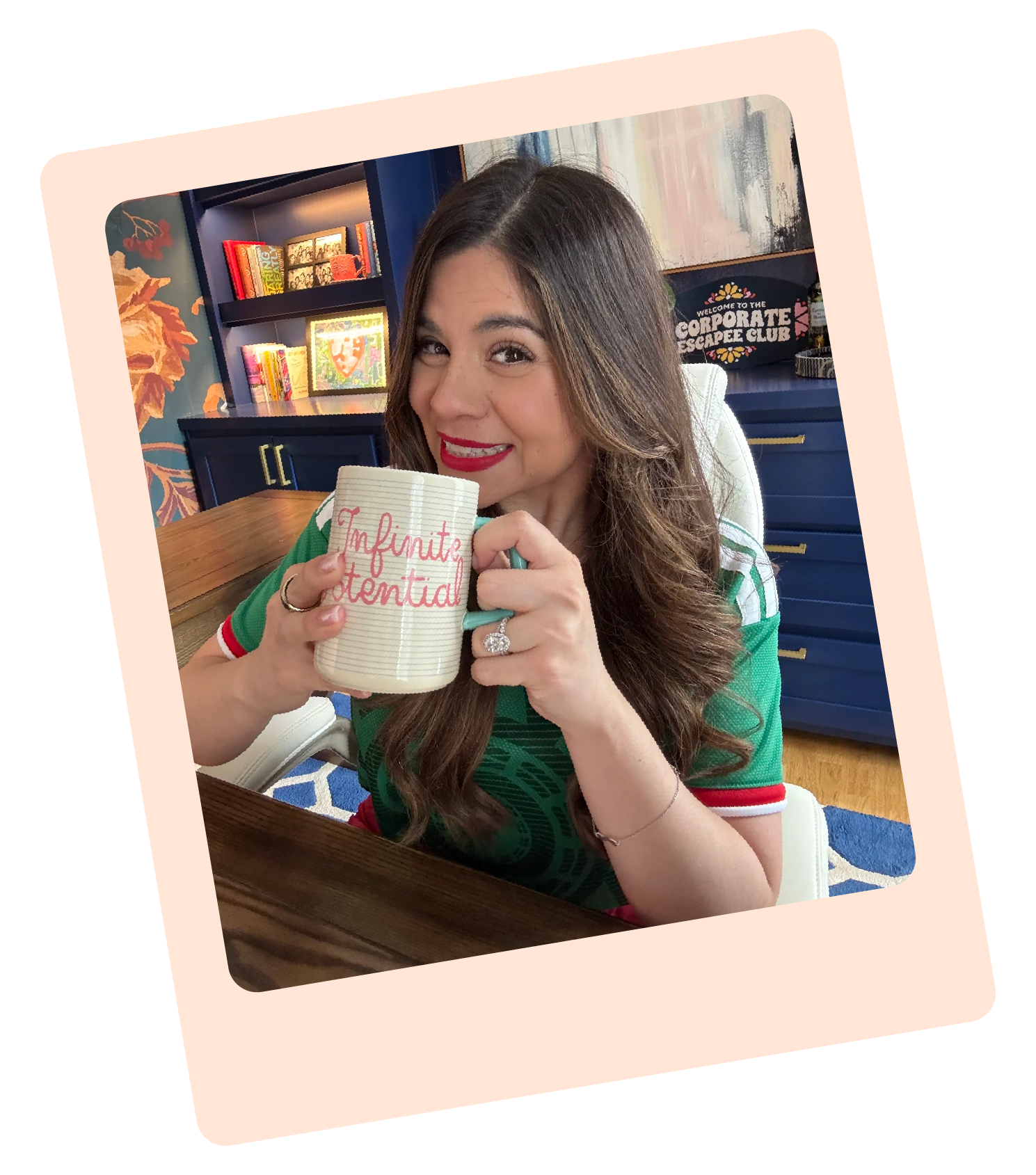 A woman with long brown hair and red lipstick sitting at a table holding a mug with the words 'Infinite Potential' written on it. She is smiling and wearing a green shirt with red and white details. In the background, there are bookshelves with colorful books and artwork, and a sign that reads 'Welcome to the Corporate Escapee Club'.