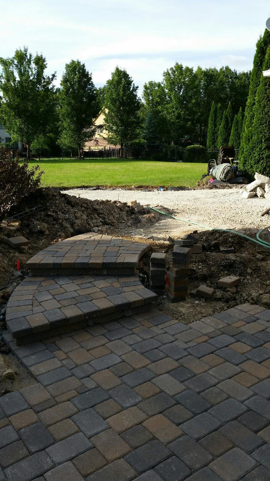 Undergoing pathway construction in a backyard, with partially completed brick pavers and a grassy lawn with trees in the background.