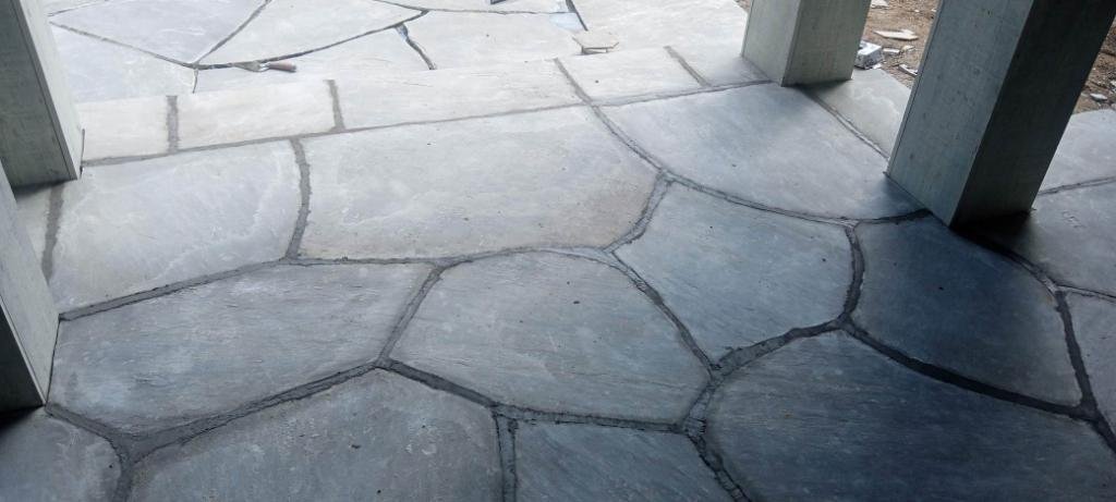 Close-up of a stone patio with irregularly shaped, grayish stones set in cement, supporting wooden structure legs.
