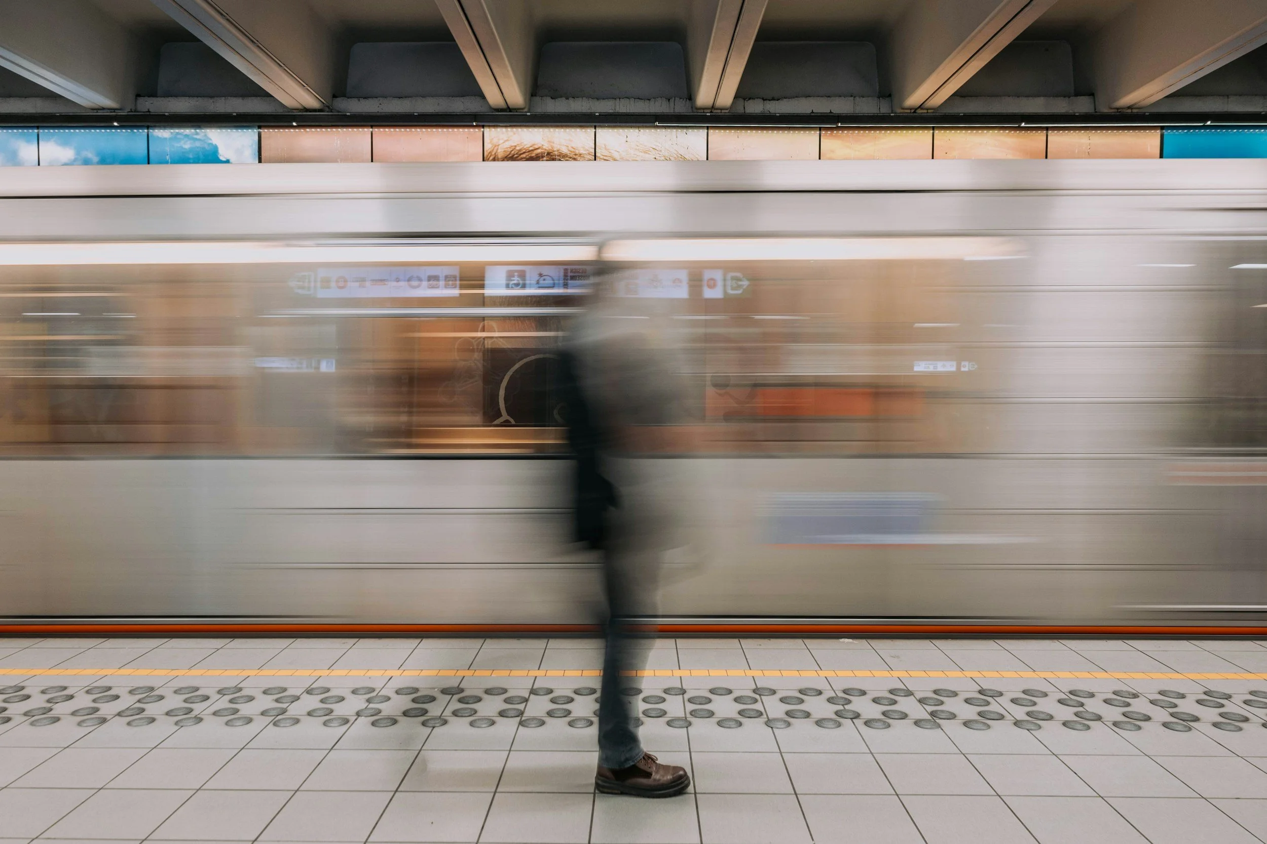 A person stands on a subway platform while a train moves past, creating a motion blur effect.