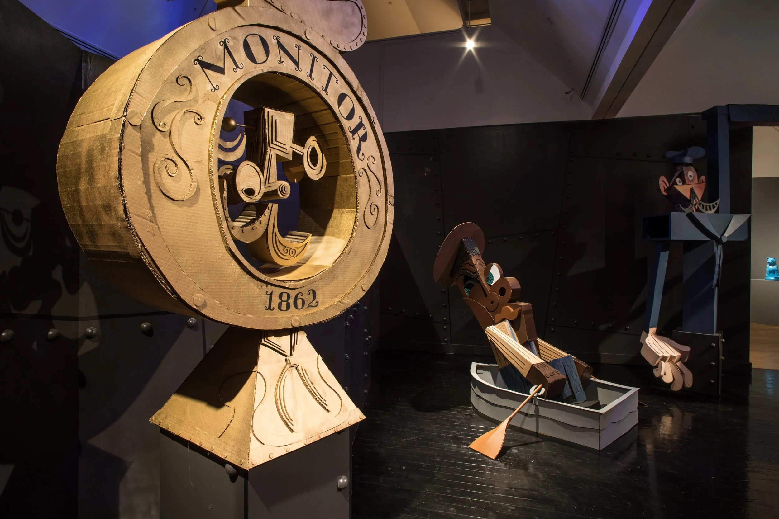 Wooden sculptures of a clock, a man with a pipe, and a man with a mustache, displayed indoors in a museum.
