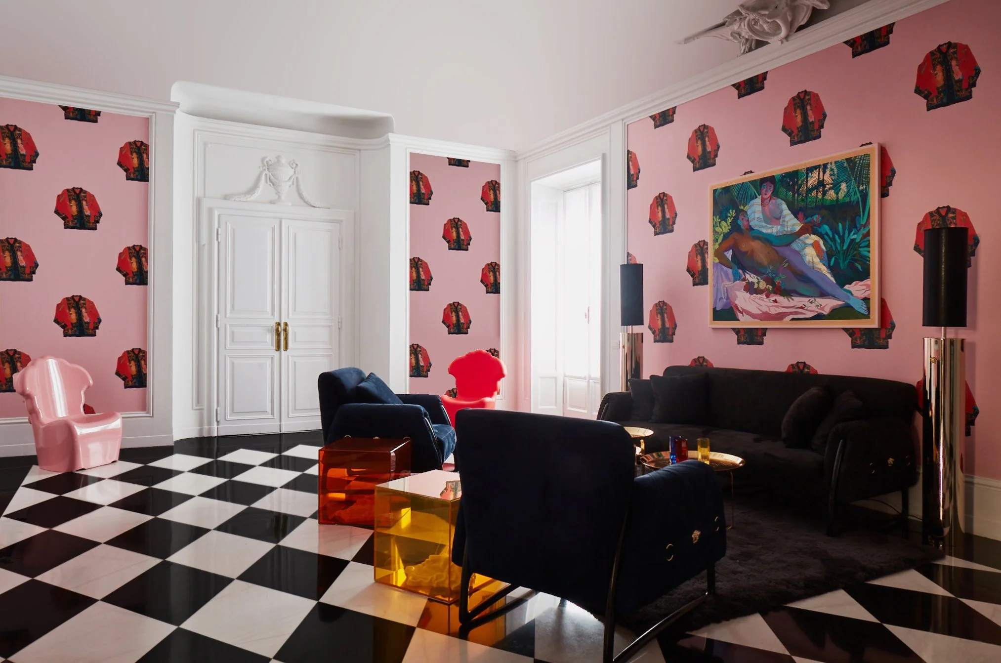 Living room with pink wallpaper featuring red and black patterned motifs, black and white checkered floor, white double doors, colorful modern furniture including black and blue sofas, pink and red chairs, and yellow and orange tables, with a large c