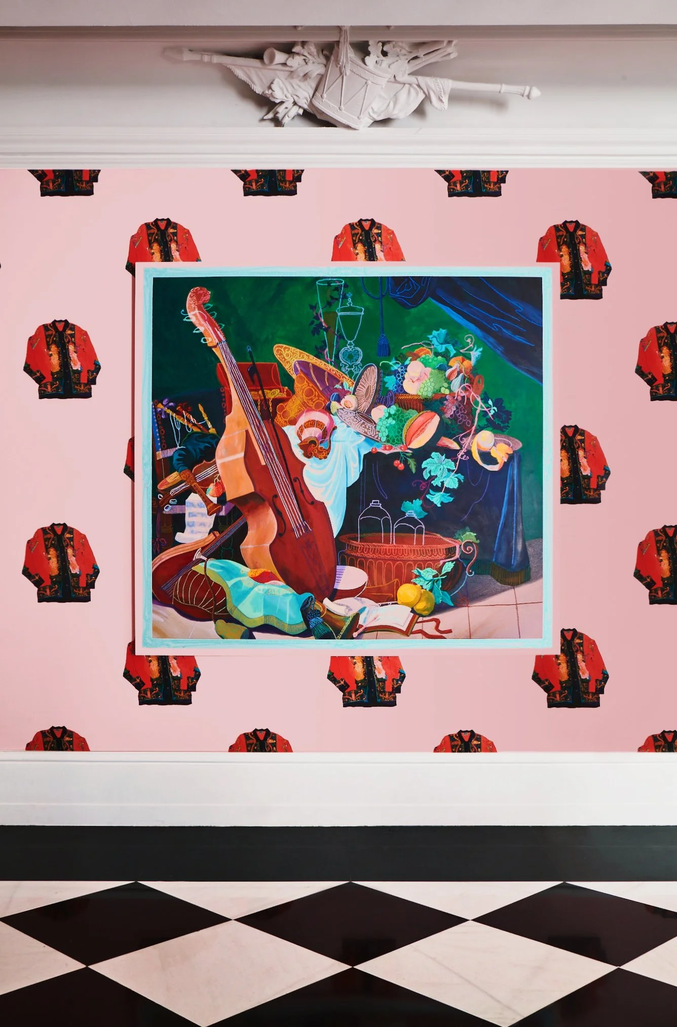 Colorful painting of musical instruments and still life objects, surrounded by patterned wallpaper with red and black jackets, in an art gallery.