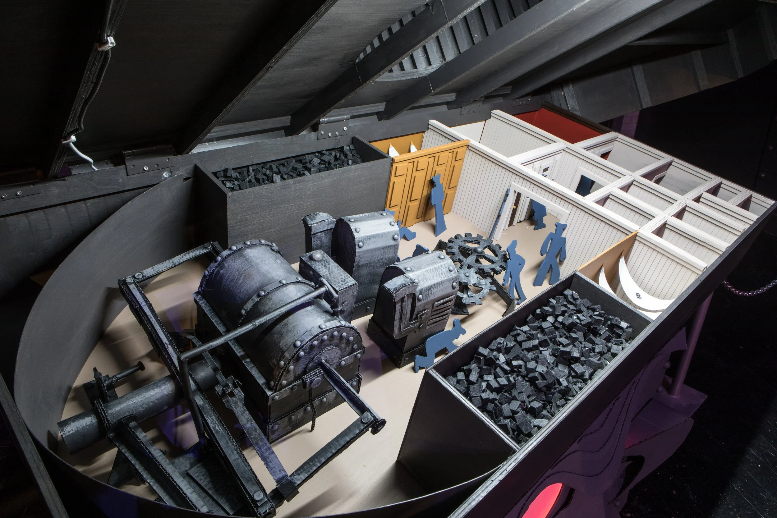 A detailed miniature model of an industrial scene with machinery, scattered gears, and stylized human figures inside a black and white painted structure.