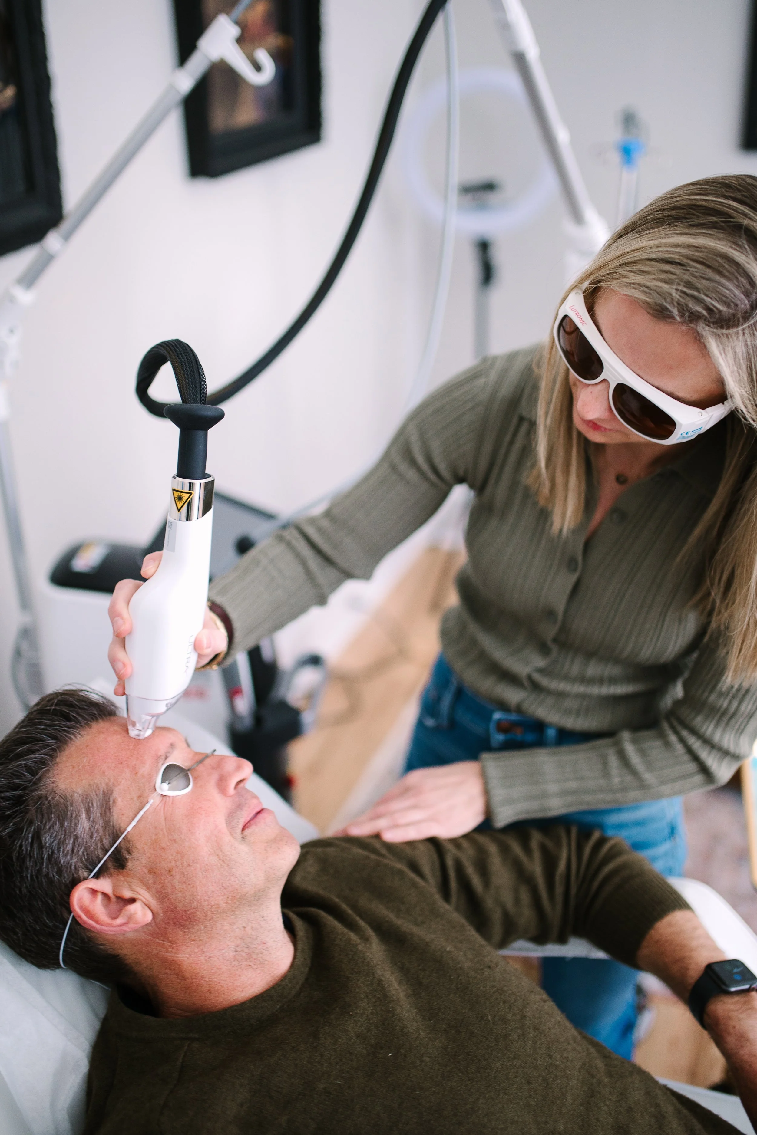 A woman receiving a laser skin treatment on her face from a technician wearing protective glasses in a clinic.