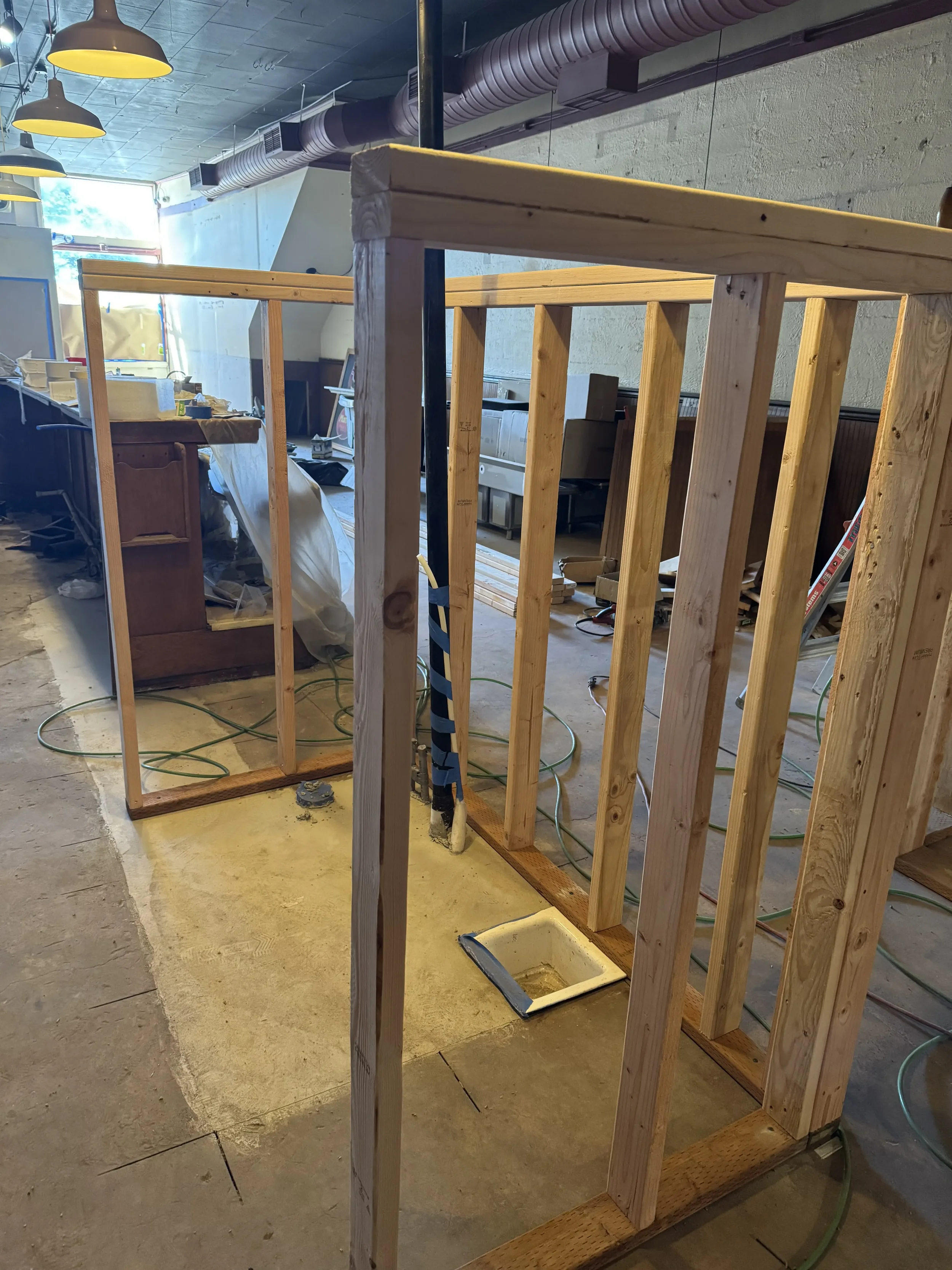 Construction site with wooden framing for a wall or partition, electrical wiring, and ductwork visible, indicating ongoing renovation or building work.