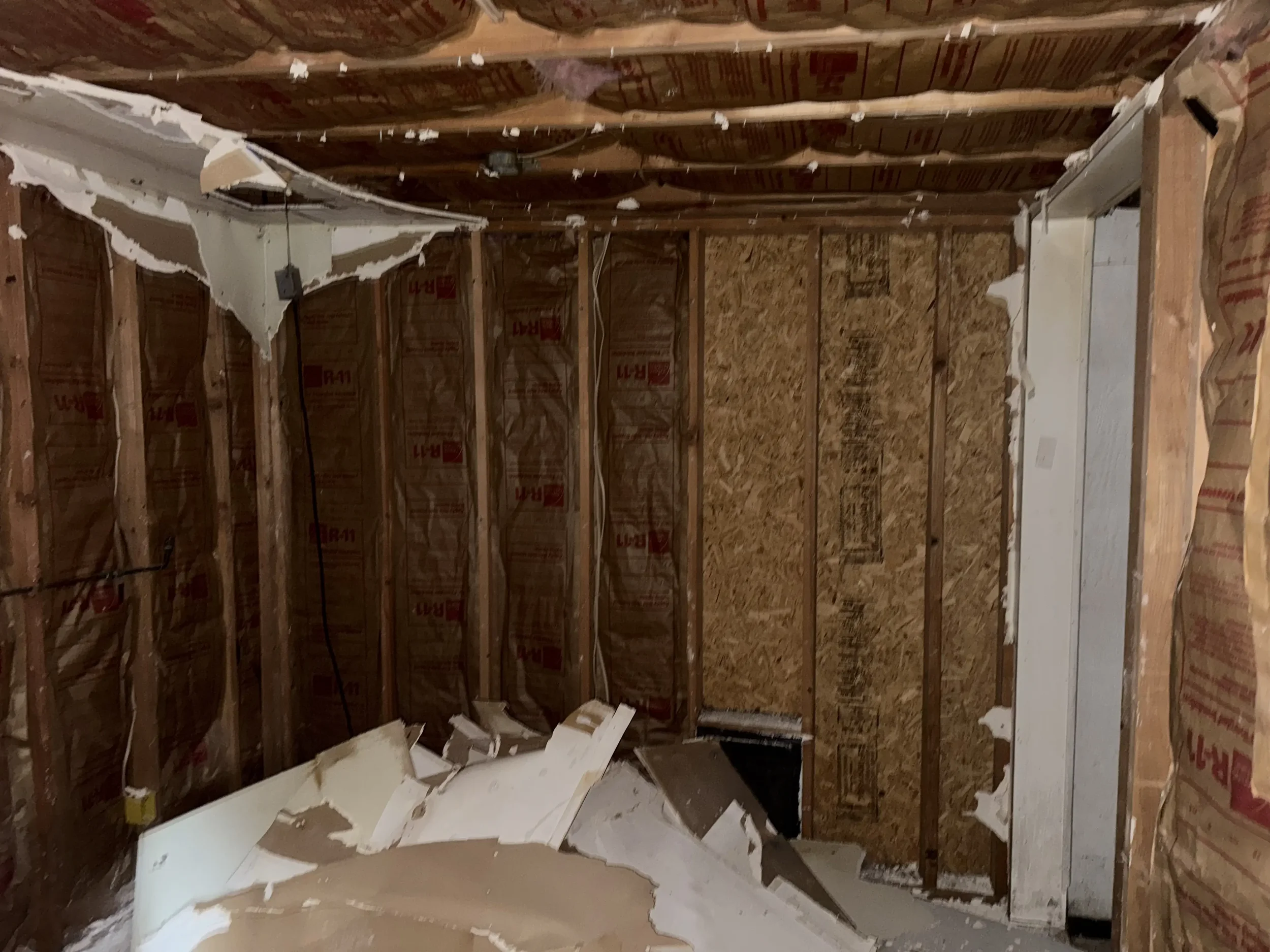 A partially demolished interior room with exposed wooden studs, insulation, and damaged drywall hanging from the ceiling and walls.