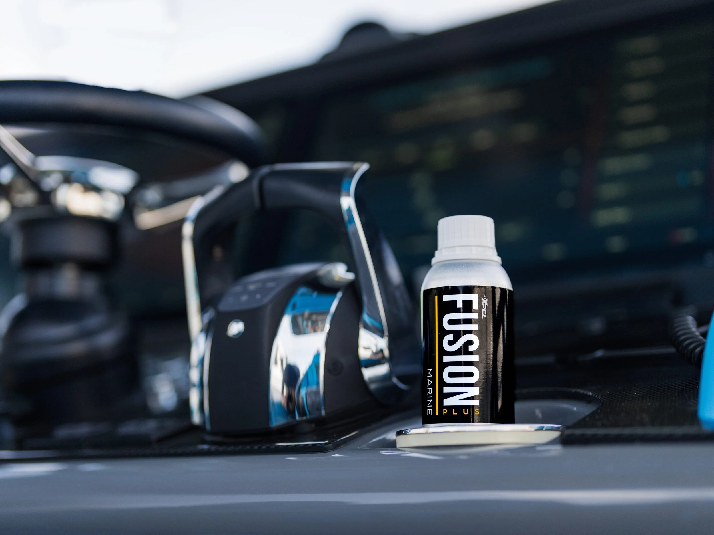 A bottle of FUSION Marine Plus fuel treatment placed on the dashboard of a vehicle, with a steering wheel and interior in the background.