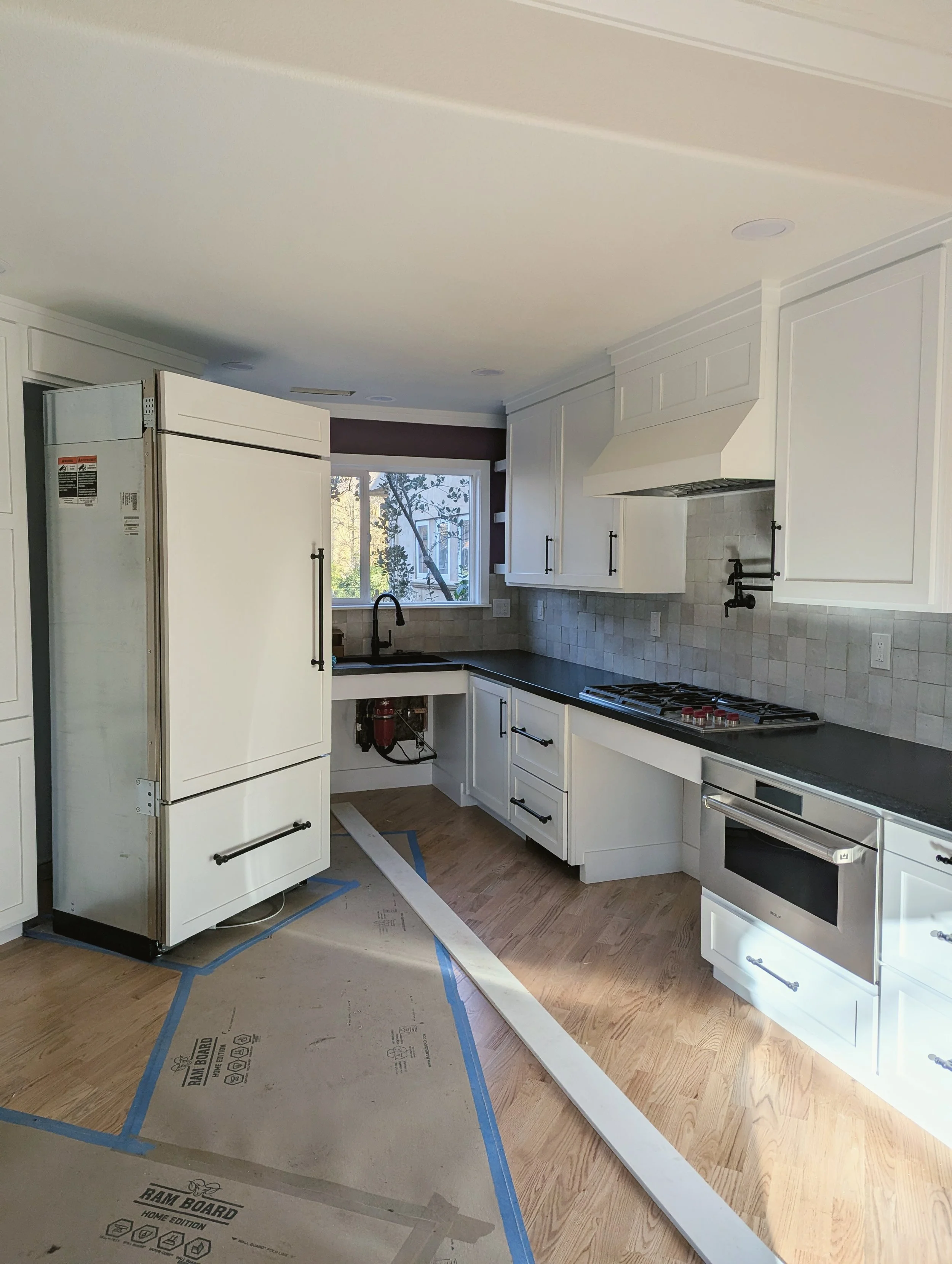 Kitchen under renovation with white cabinets, a black countertop, a stove, and a window with trees outside.
