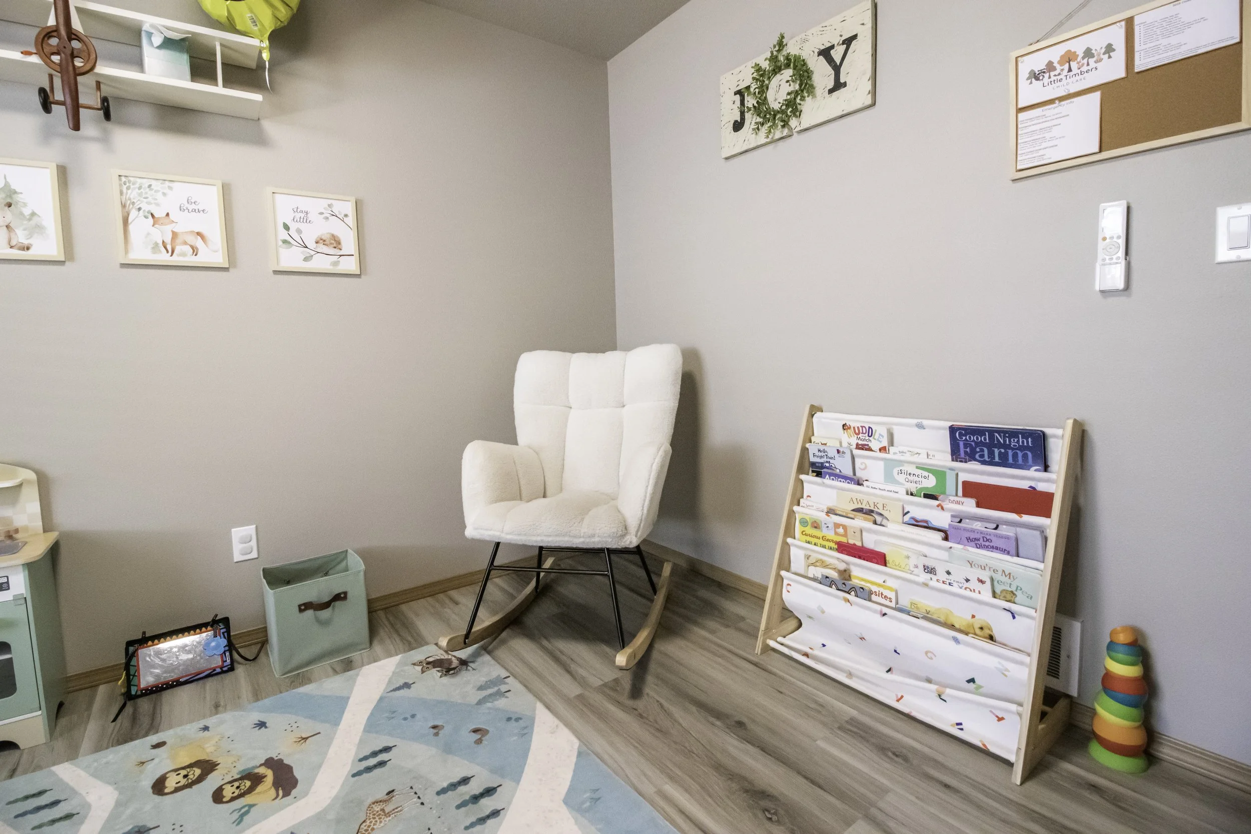 A cozy reading corner in a child's room with a white rocking chair, a bookshelf filled with children's books, and decorative framed art on the walls.