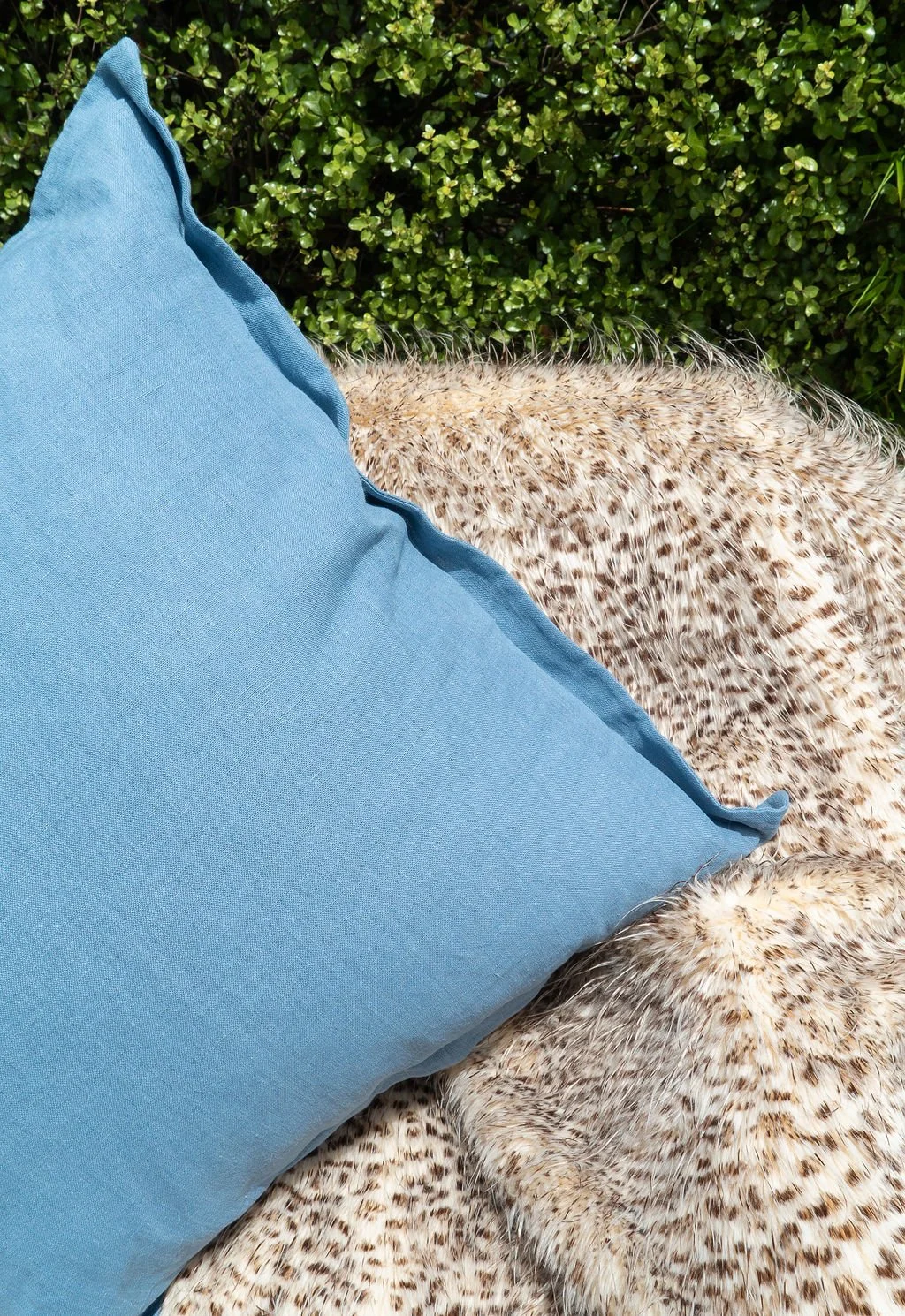 A close-up of a light blue outdoor pillow resting on a speckled animal fur blanket.