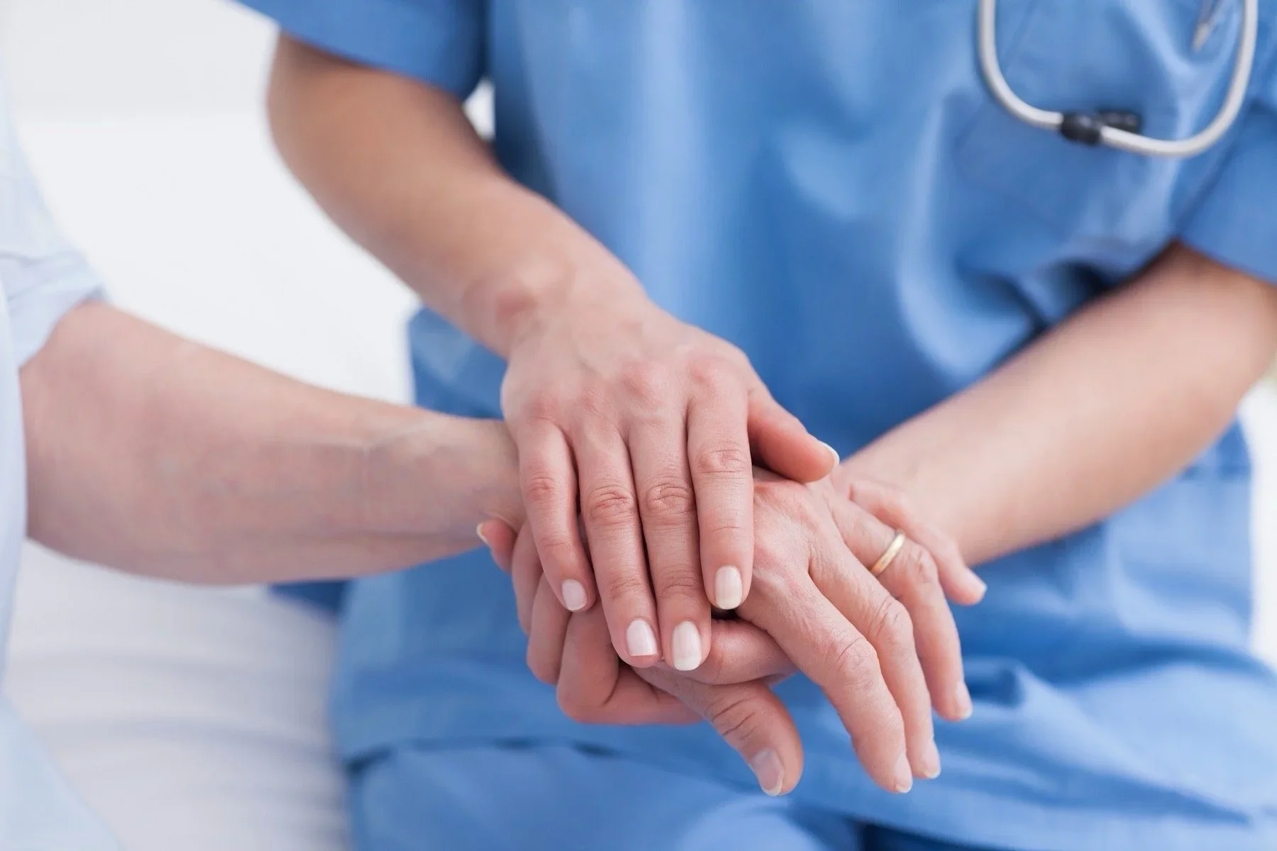 A healthcare professional in blue scrubs is gently holding an elderly patient's hand, symbolizing care and compassion.