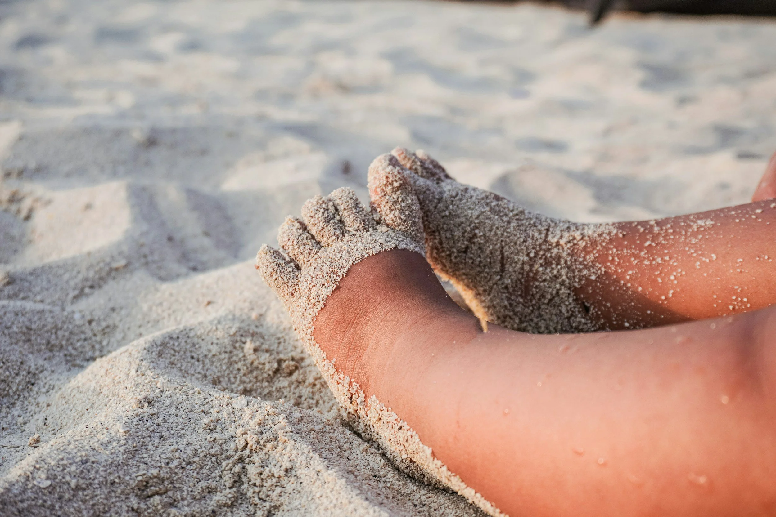 Close-up of a person's leg and foot covered in sand lying on a sandy beach.