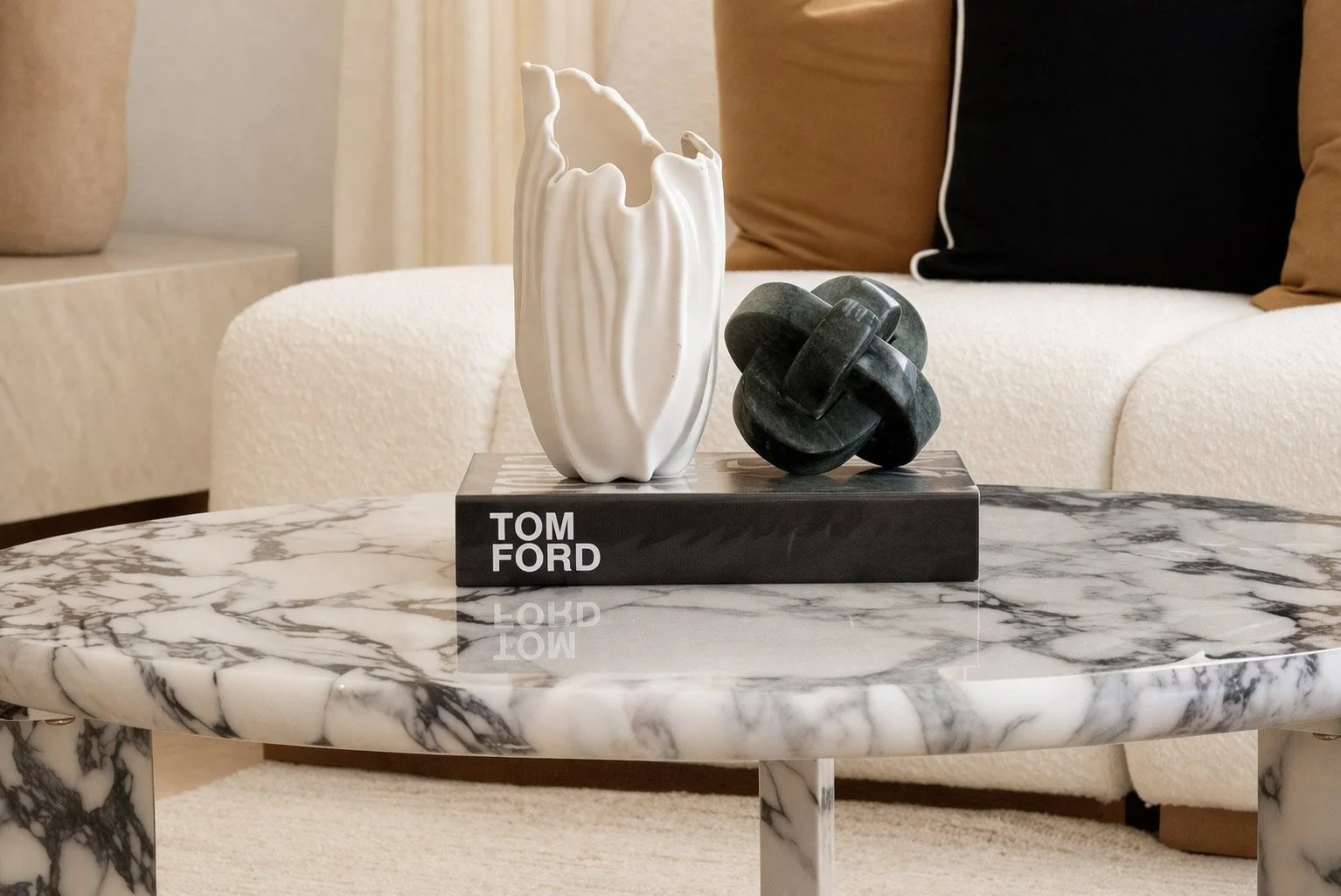 Decorative sculpture featuring a white ceramic piece and a black tangled ring on a black base reading 'Tom Ford', placed on a white marble table.