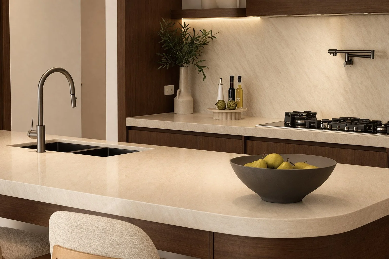 Modern kitchen with beige countertop, dark wood cabinets, sink with tall faucet, bowl of green pears, and decorative bottles on the counter.