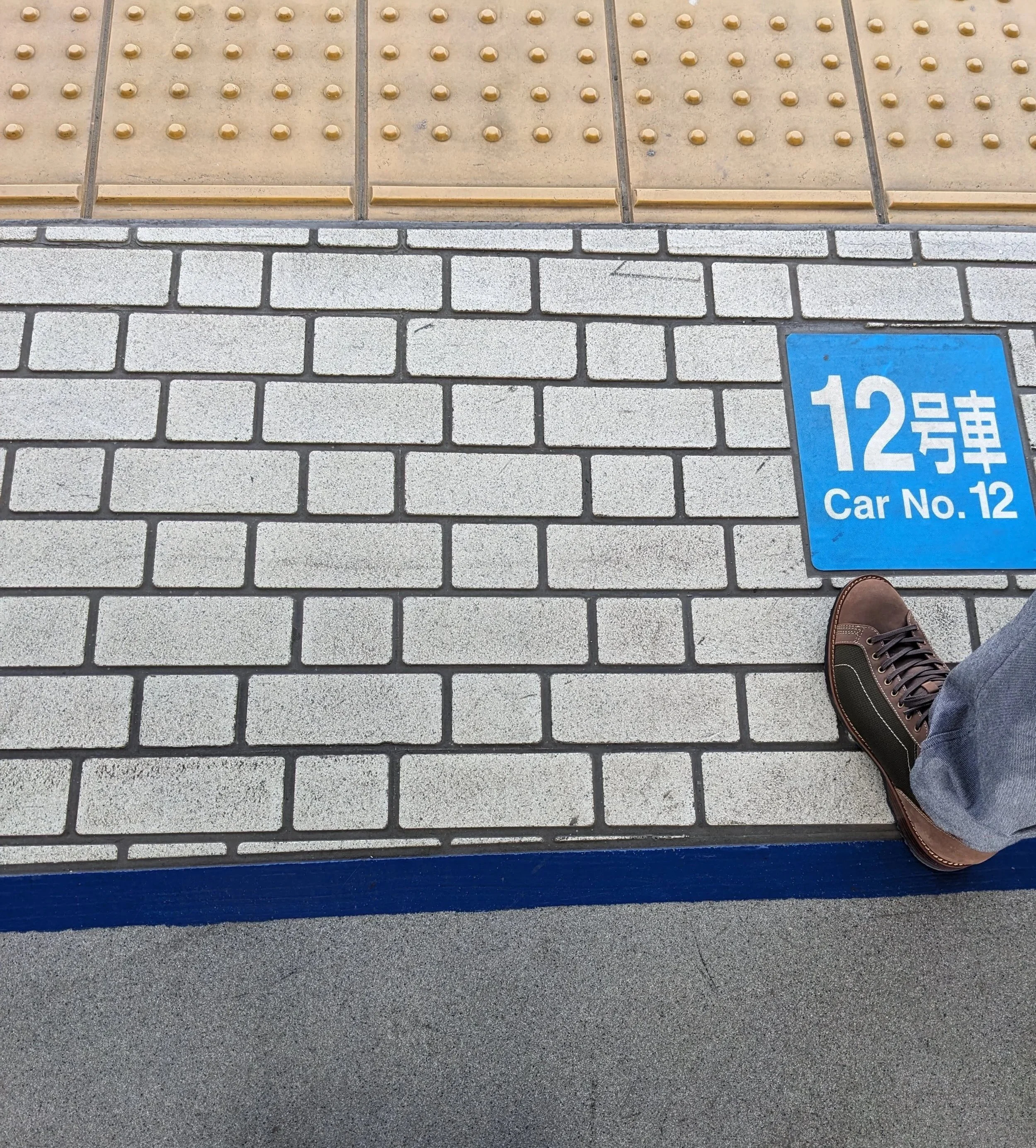 two pairs of feet in line to board next to a sign that says that train car 12 will pull up here