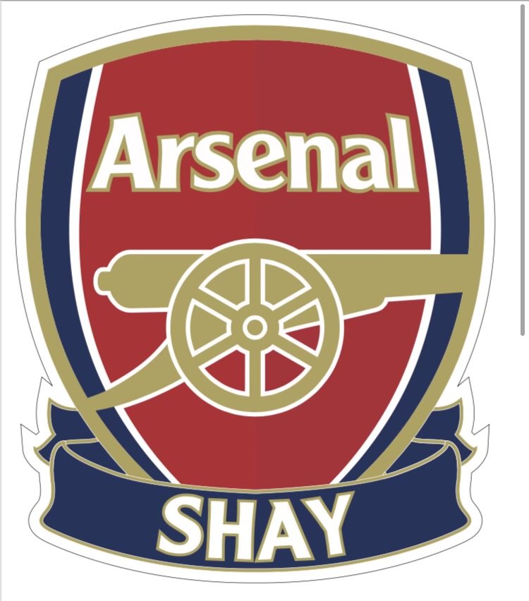 A crest featuring a red shield with a gold cannon and the words 'Arsenal SHAY' in gold and white text.