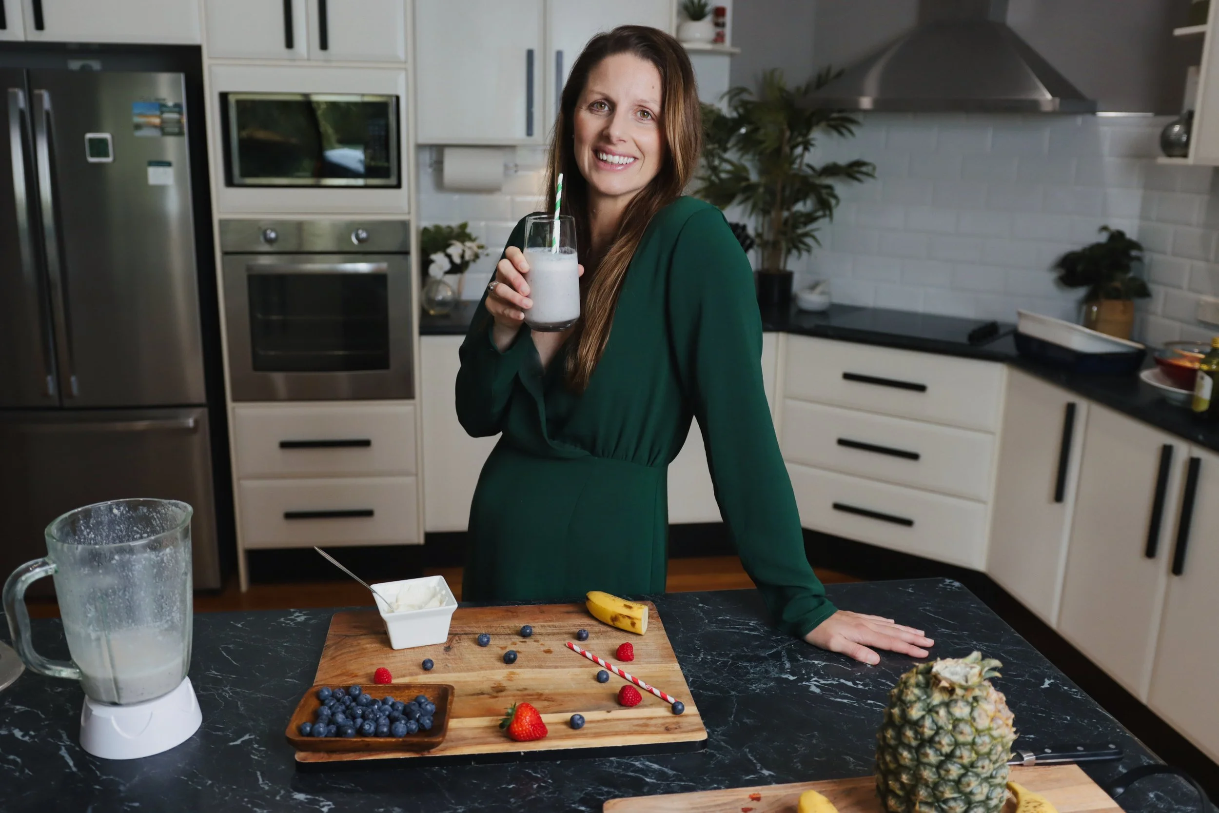 Ashleigh Brunner Sports Dietitian in Sydney standing in her kitchen for a Sports Nutrition Workshop with various healthy smoothie ingredients infront of her