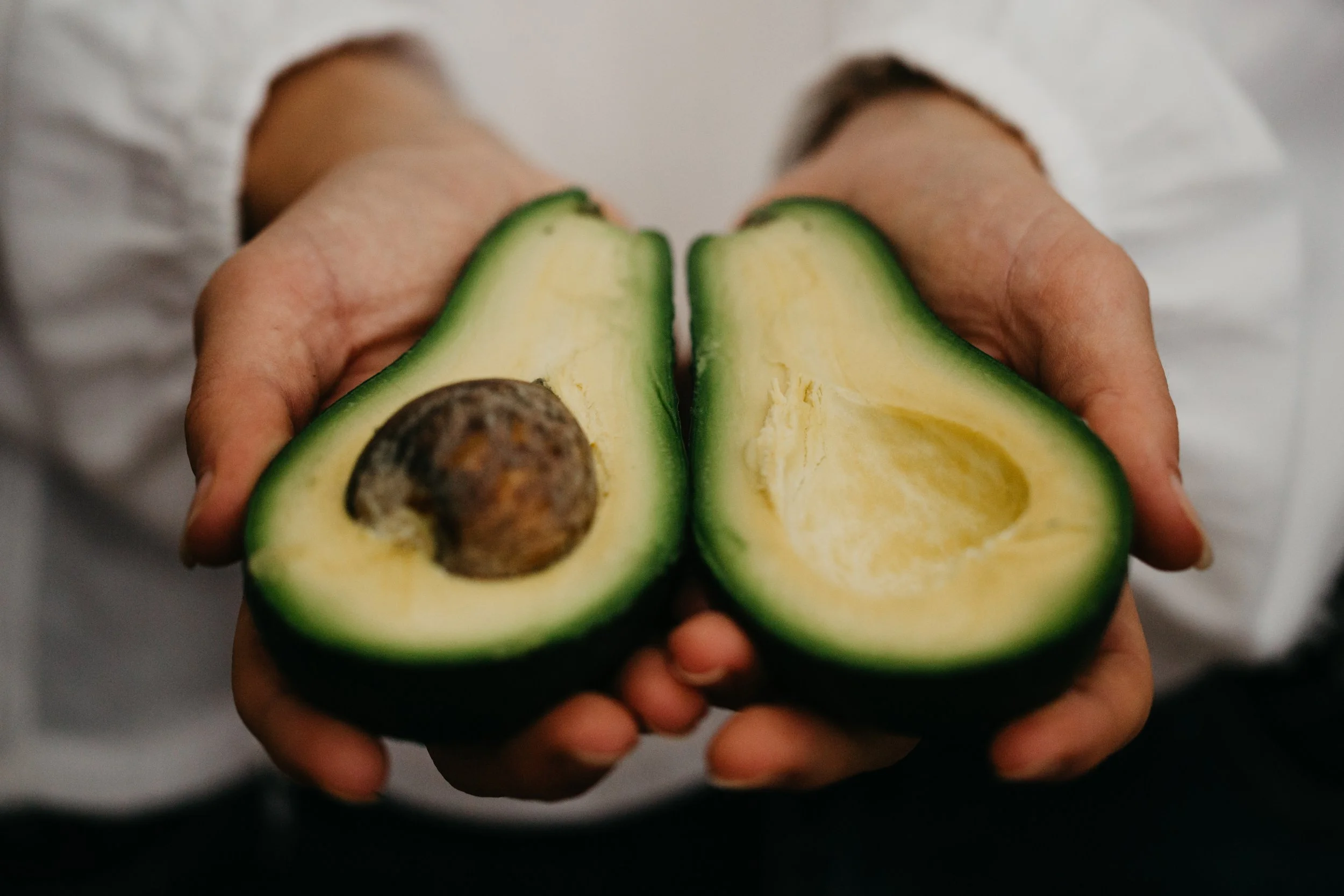 Sports Dietitian holding a halved avocado, showing the seed on one side and the empty seed cavity on the other.