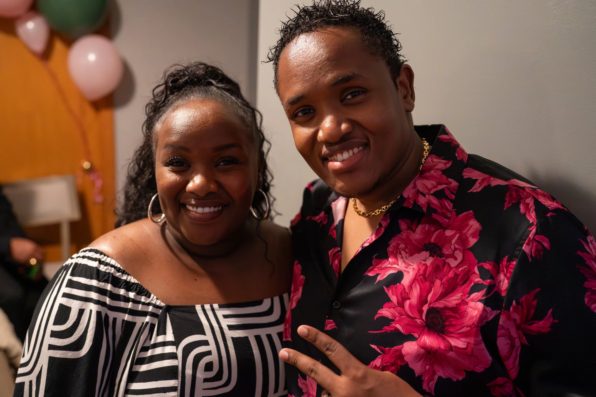 A smiling woman and a smiling man posing together at a party, with balloons in the background.