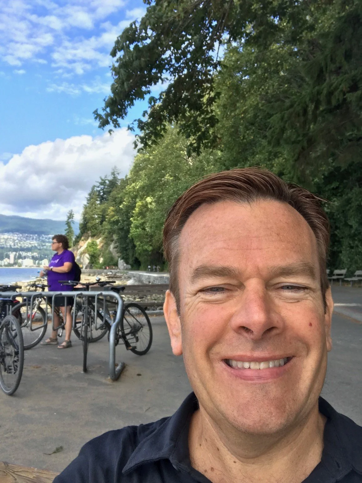 A man smiling in a white shirt standing inside an empty football stadium.