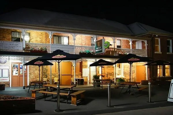 Outdoor seating area with picnic tables and umbrellas in front of a brick building at night.