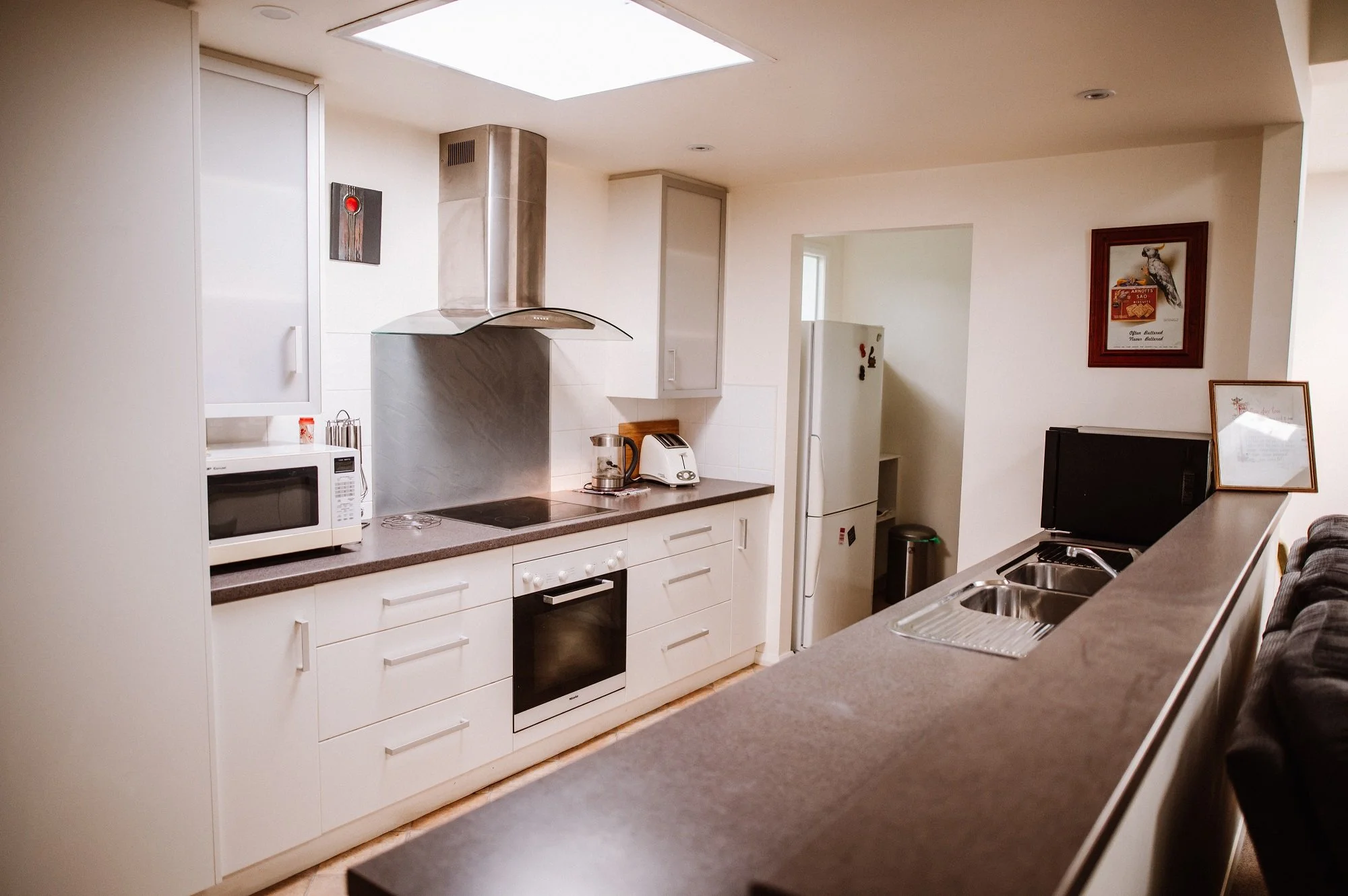 Kitchen with white cabinets, black countertop, microwave, oven, range hood, refrigerator, toaster, kettle, and framed artwork on the wall.