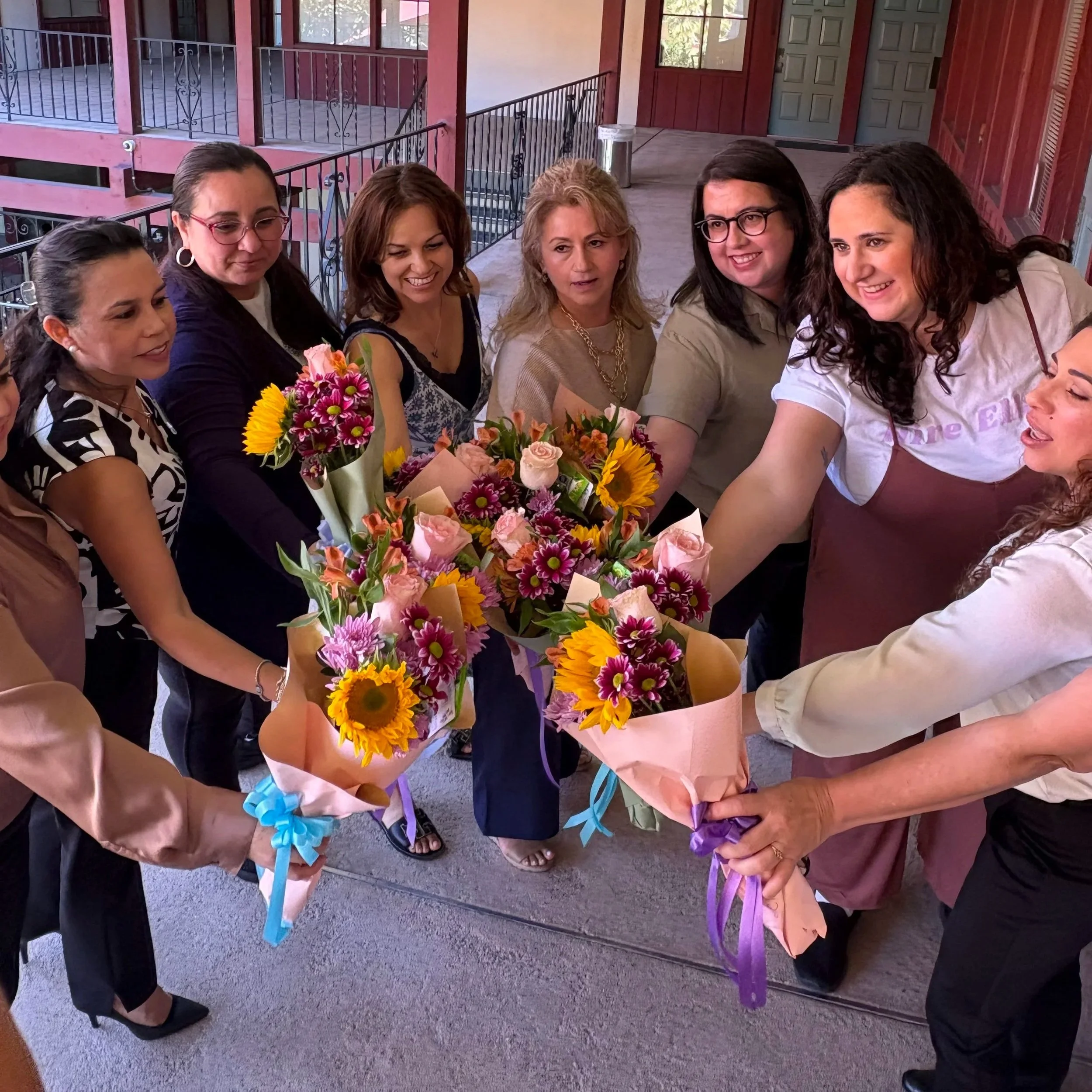 A group of women gathering around to celebrate with multiple colorful flower bouquets.
