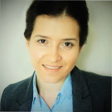 Headshot of a woman with short dark hair, wearing a blue collared shirt and a dark blazer, smiling at the camera.