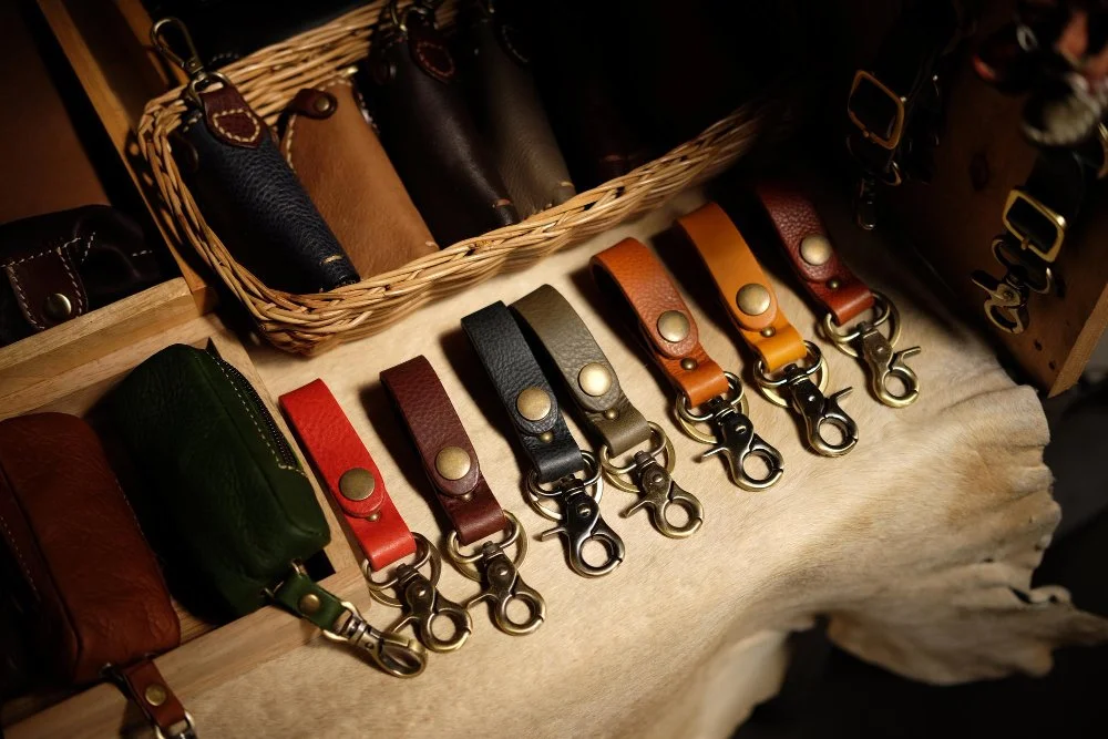 Display of leather keychains in various colors arranged on a table with a basket of more keychains in the background.