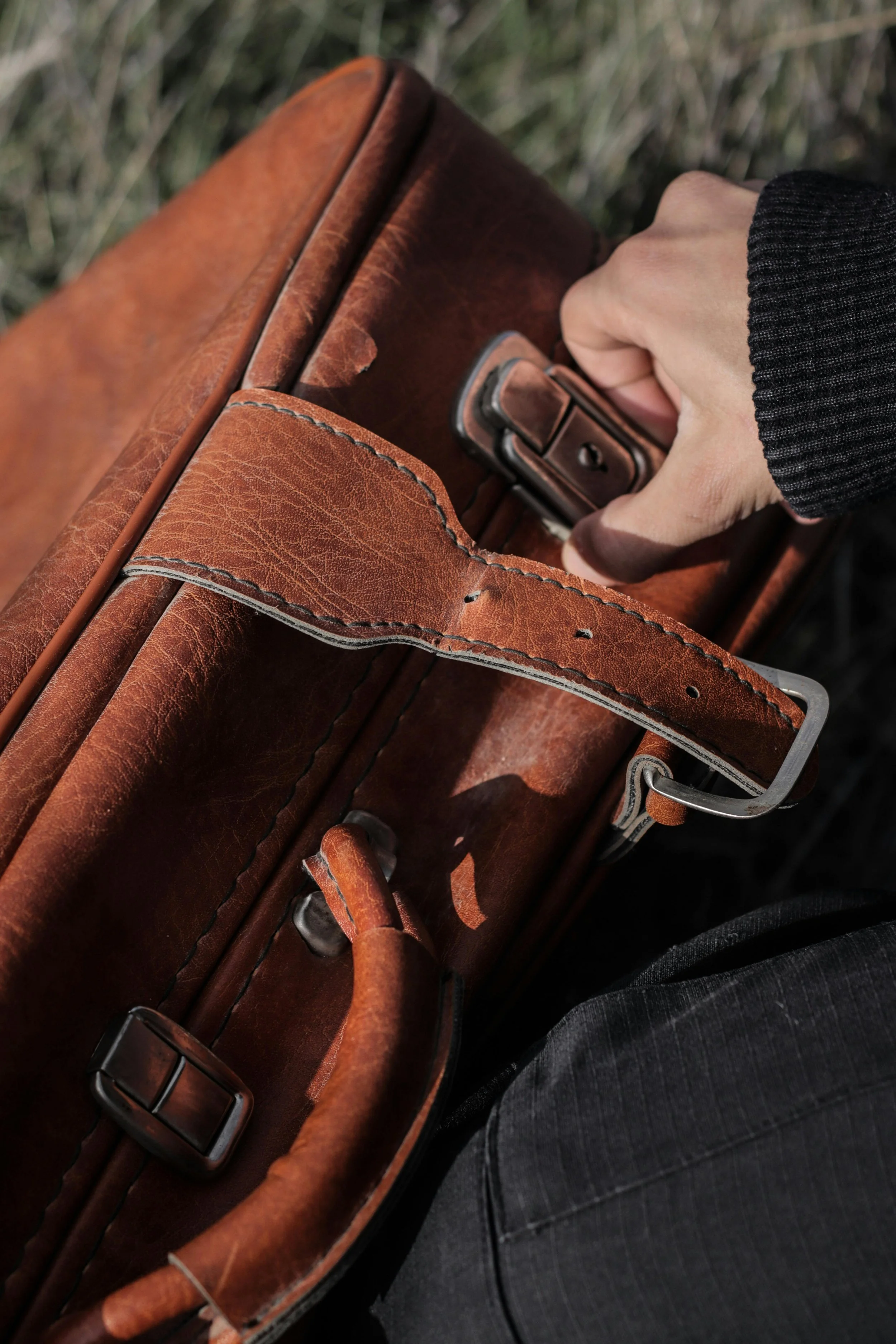 A hand gripping the handle of a worn, brown leather briefcase.